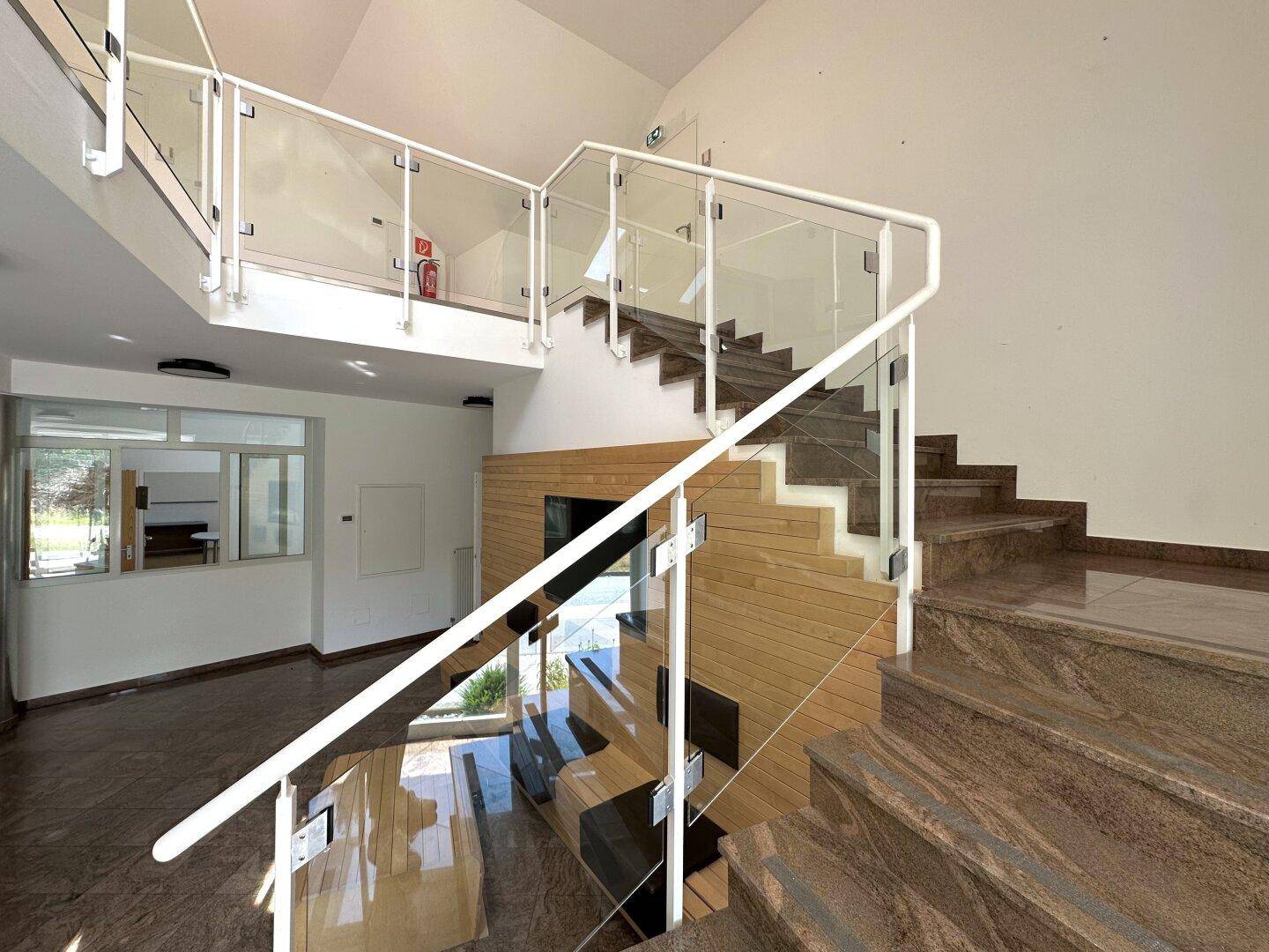 Moderne Treppe mit Glasgeländer und Marmorstufen in einem hellen, einladenden Eingangsbereich.