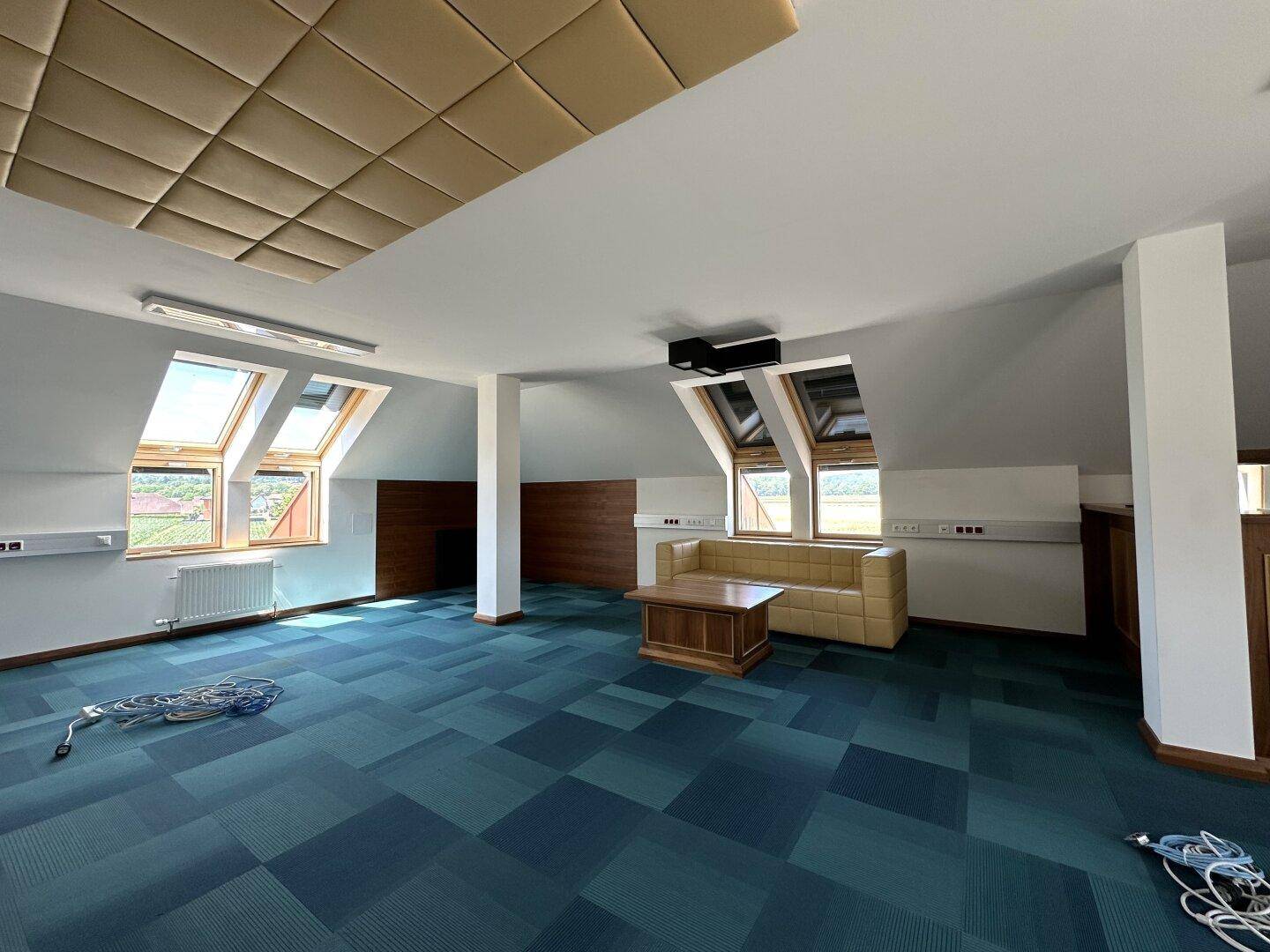 Heller Loungebereich im Dachgeschoss mit Sofa, Holztisch und schrägen Dachfenstern für viel Licht.
