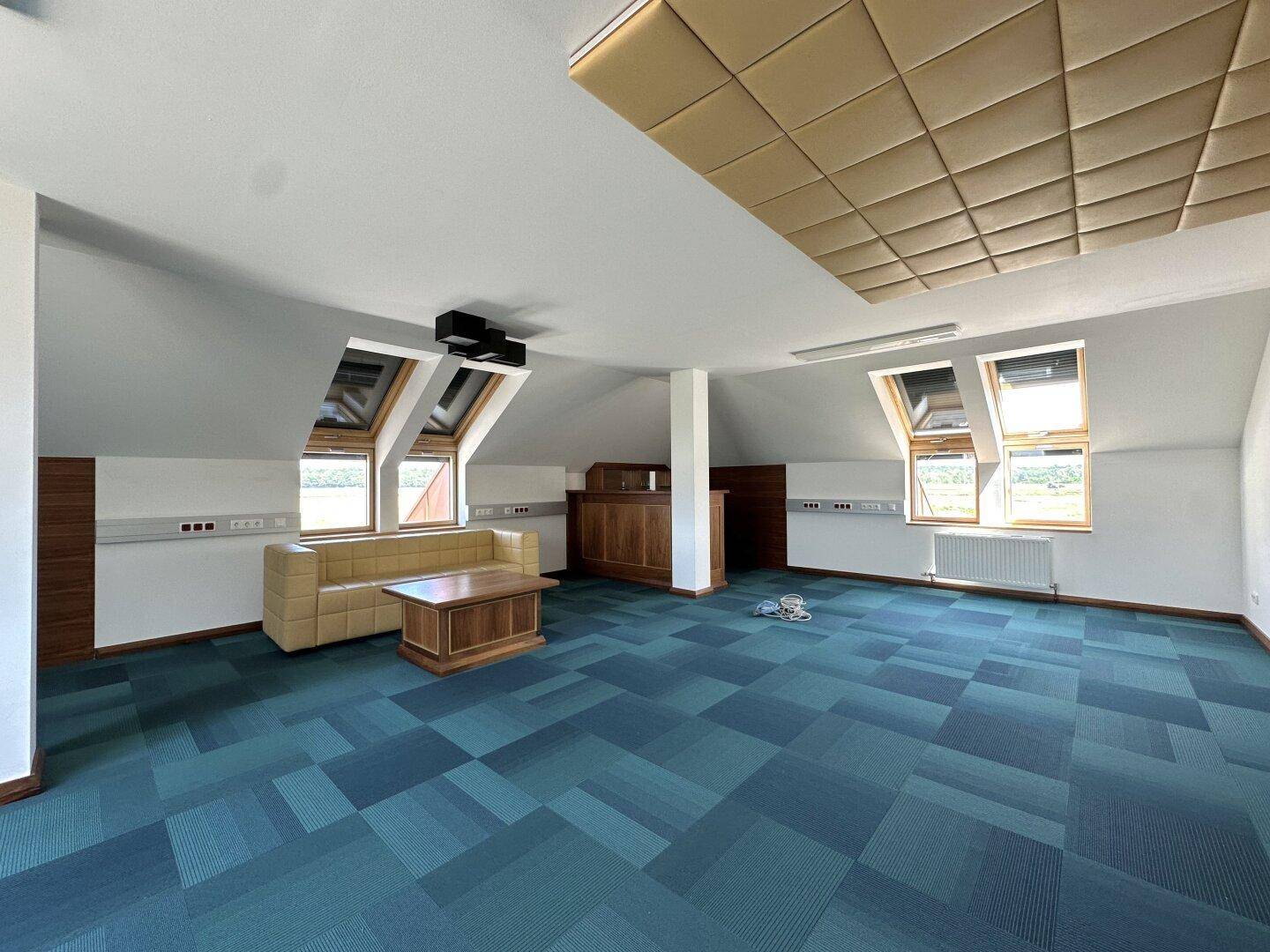 Gemütlicher Loungebereich im Dachgeschoss mit gemustertem Teppich, Sofa und schallabsorbierenden Deckenplatten.