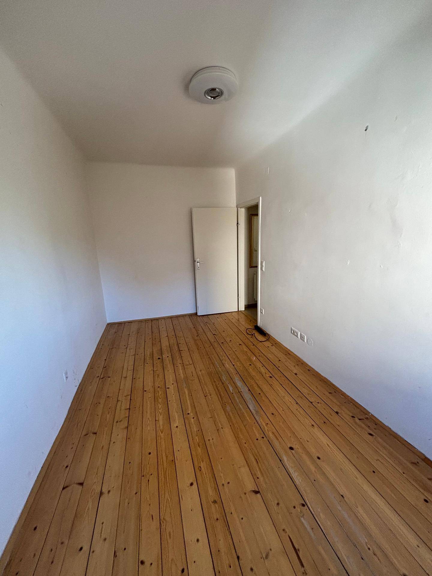 Leeres Schlafzimmer mit warmem Holzdielenboden und einer Tür, bereit zur individuellen Gestaltung.