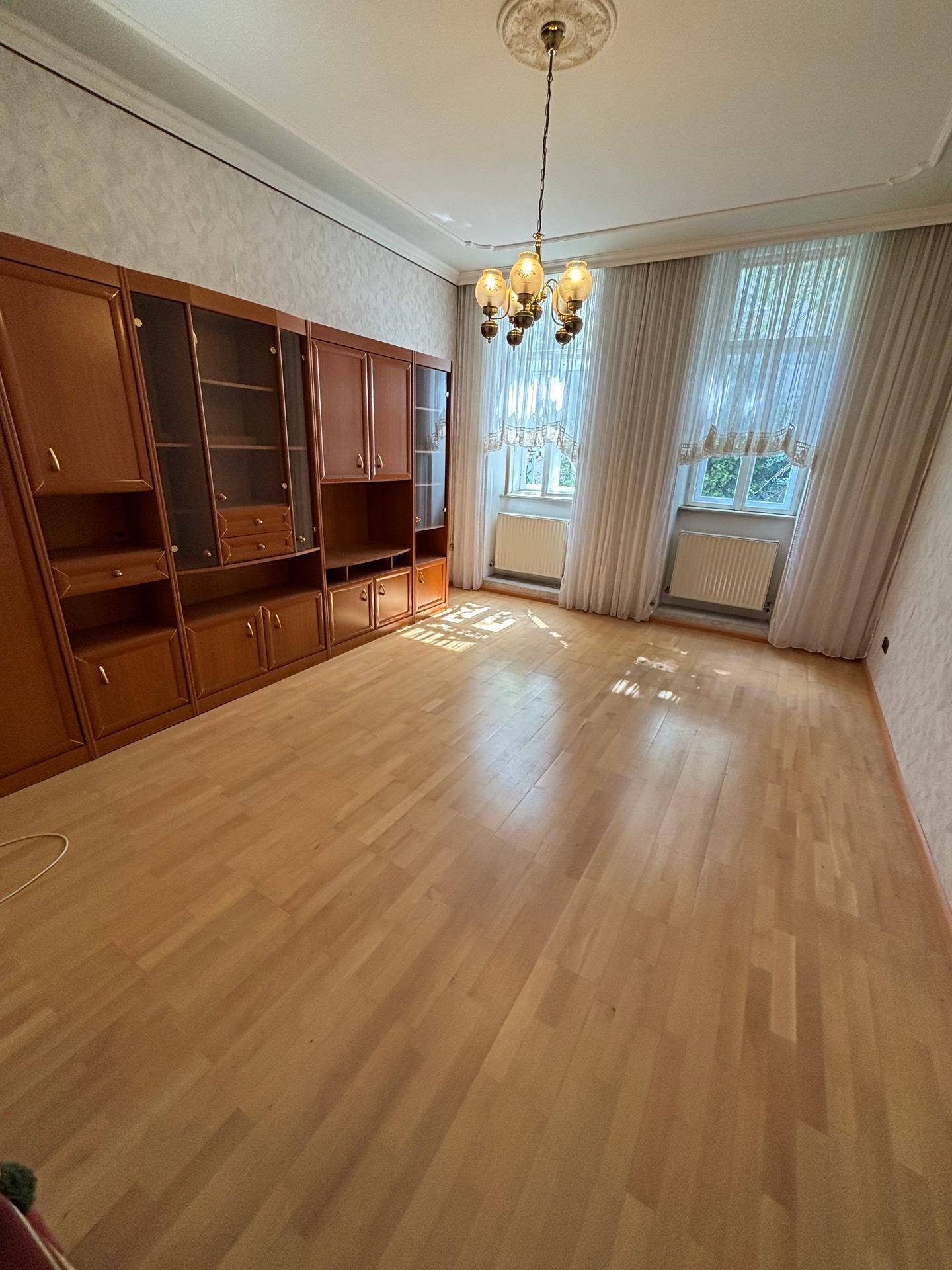 Geräumiges Wohnzimmer mit Parkettboden, Stuckdecke und großen Fenstern für viel Tageslicht.