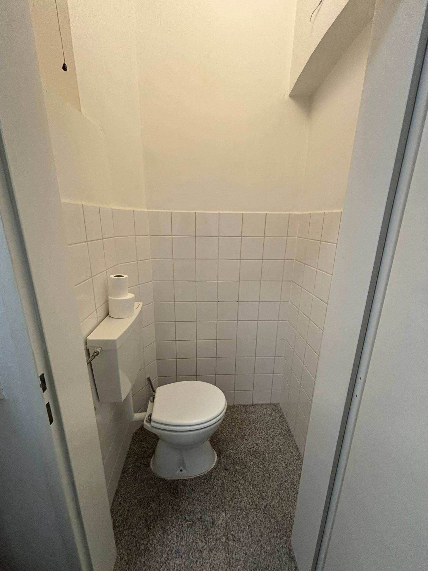 Kleiner Toilettenraum mit WC, weißen Wandfliesen und grauem Fliesenboden.