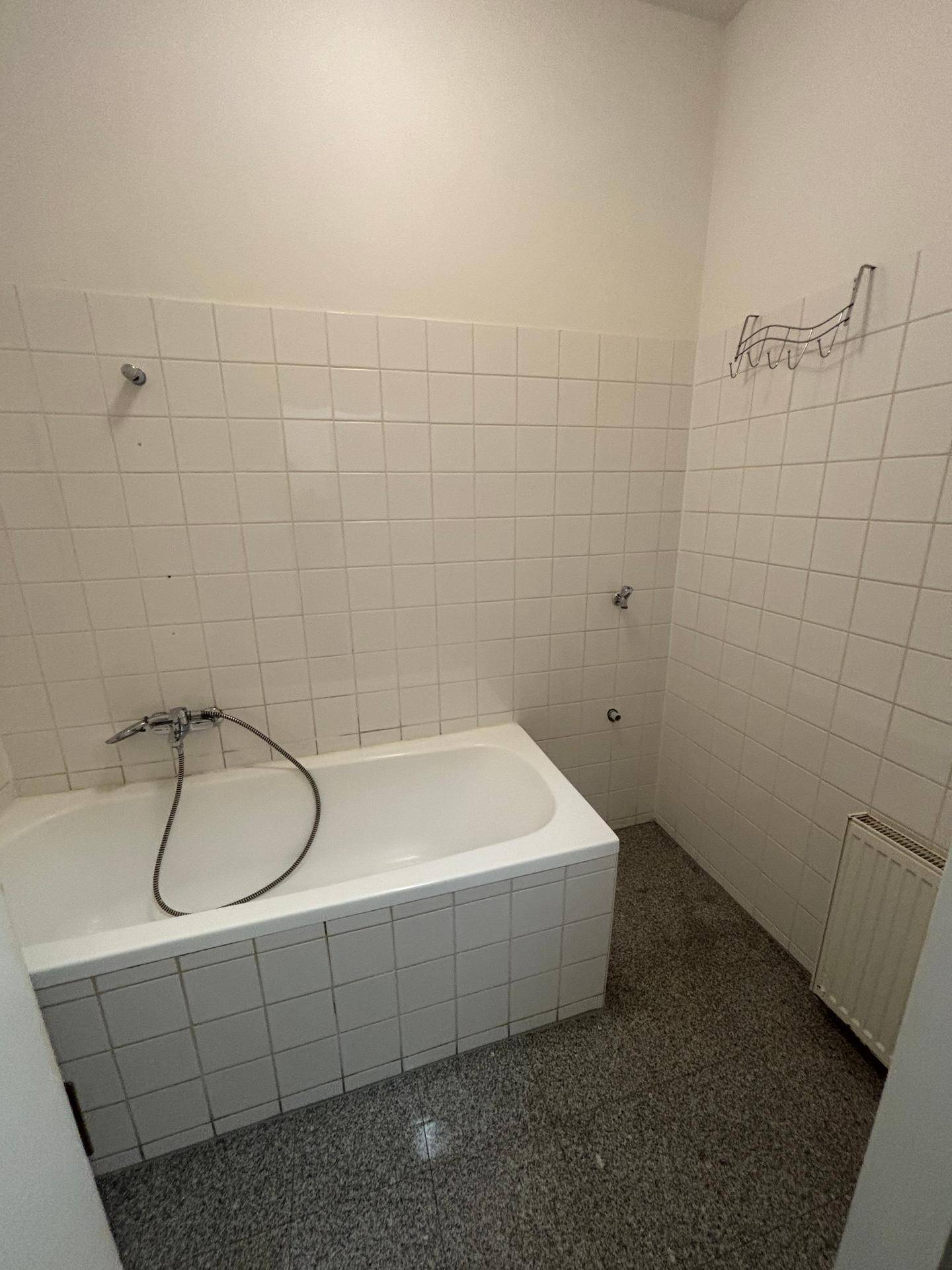 Badezimmeransicht mit Badewanne, weißen Wandfliesen, grauem Fliesenboden und Heizkörper.