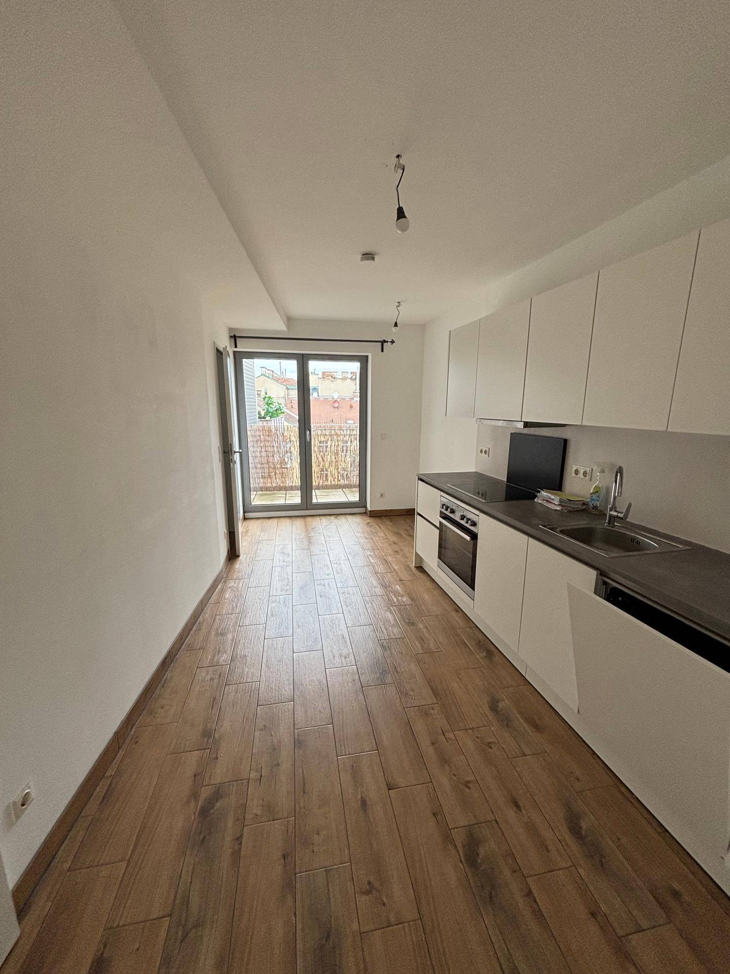 Heller Küchenbereich mit weißen Einbauschränken und Zugang zu einem Balkon durch eine Glastür.