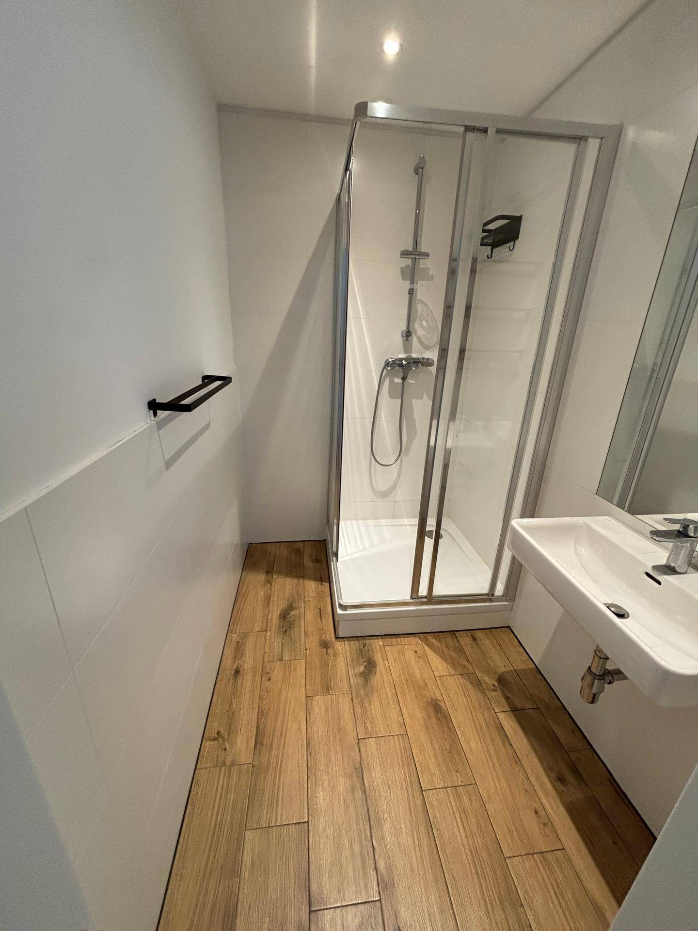 Modernes Badezimmer mit Duschkabine, Waschbecken und Holzboden in heller Optik.