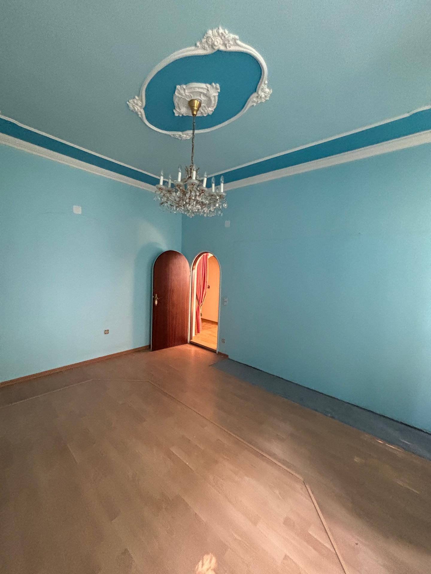 Zimmer mit blauen Wänden, Parkettboden und einer dekorativen Deckenrosette mit Kronleuchter.