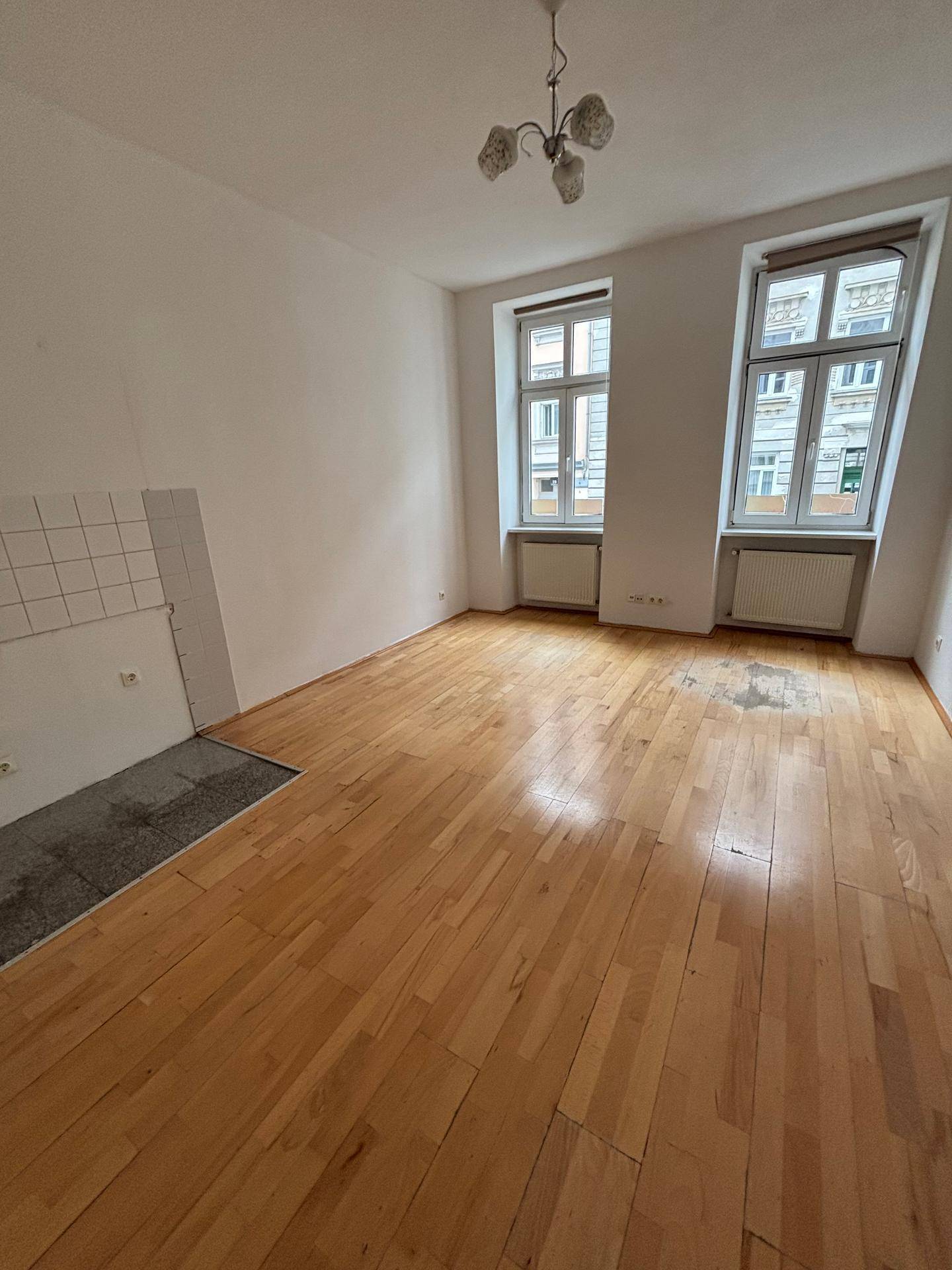 Heller Wohnraum mit Holzplankenboden, zwei großen Fenstern und Blick auf die Straße.