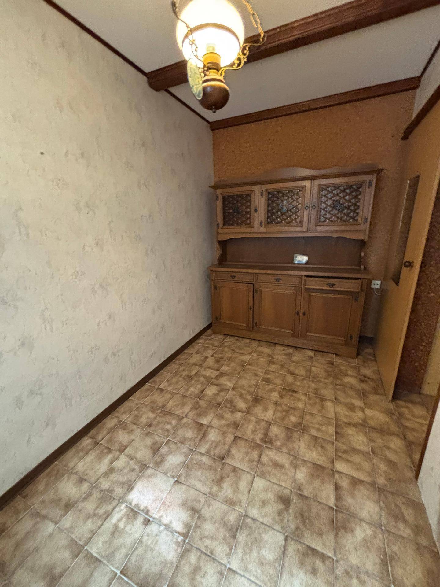 Zimmer mit Fliesenboden, Holzbalken an der Decke und einem traditionellen Holzschrank.