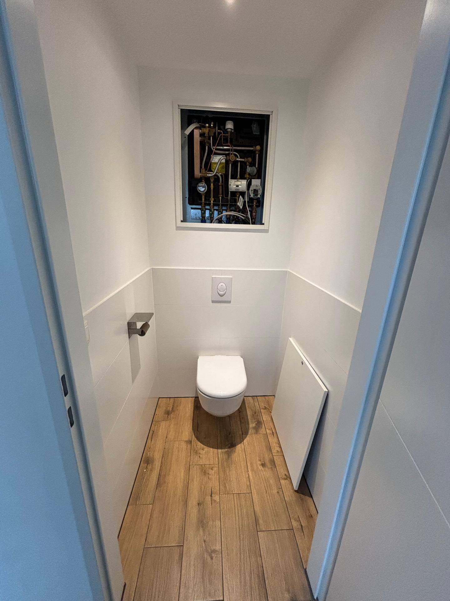 Separates WC mit wandhängender Toilette und sichtbaren Installationen im oberen Bereich.