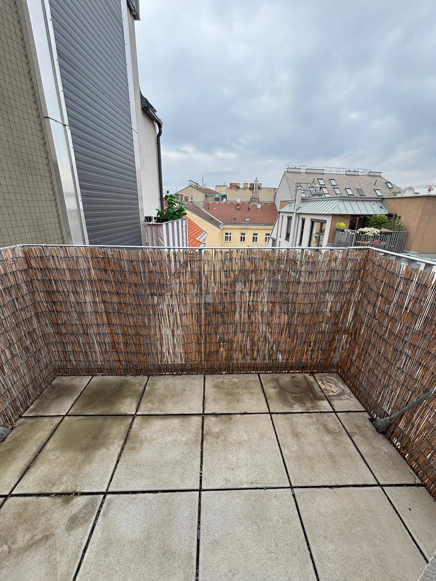 Balkon mit Fliesenboden und Bambus-Sichtschutz, bietet einen Blick auf die umliegenden Gebäude.