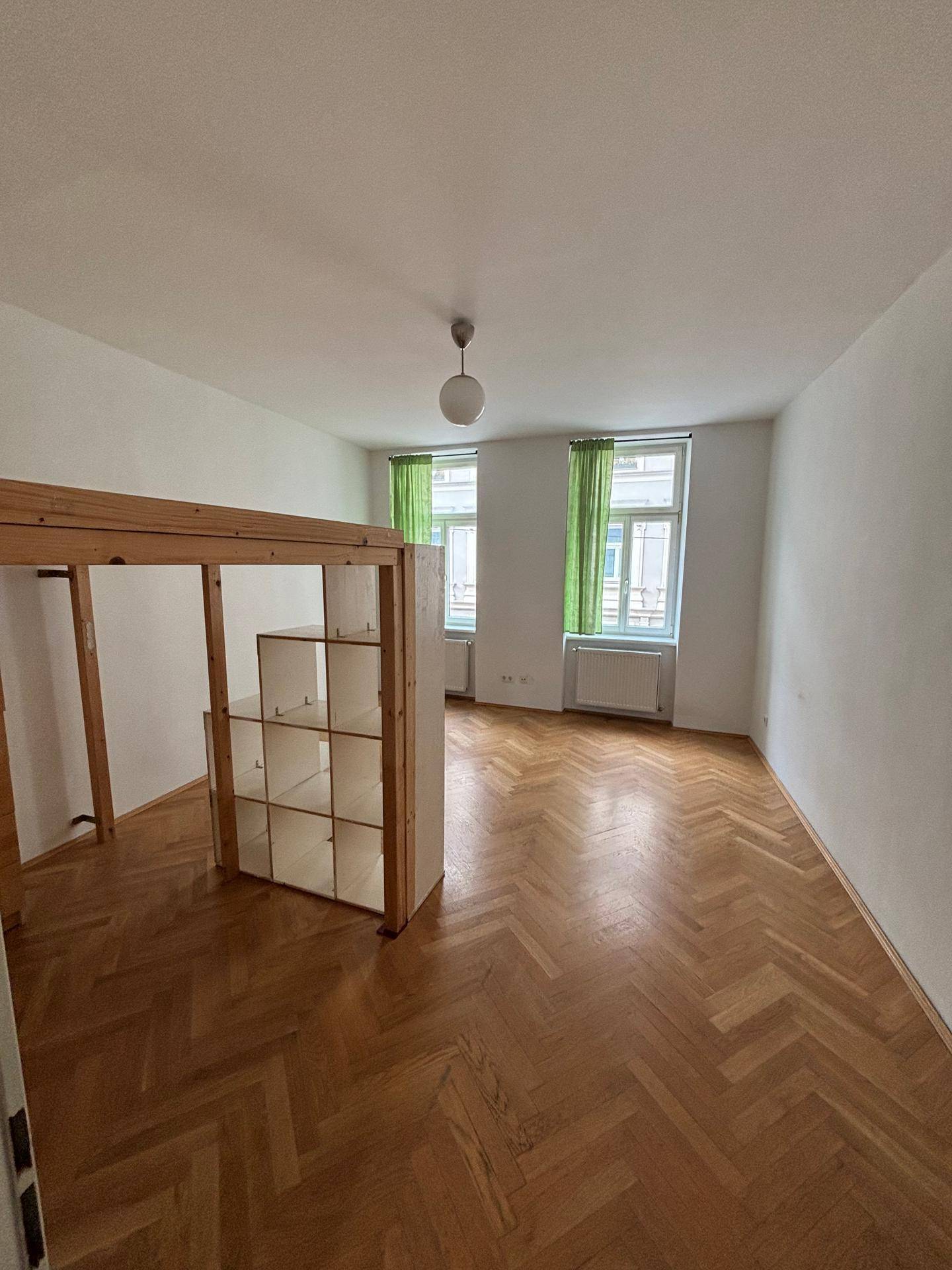 Geräumiges Zimmer mit Fischgrätparkett, zwei Fenstern und einer praktischen Hochbettkonstruktion.