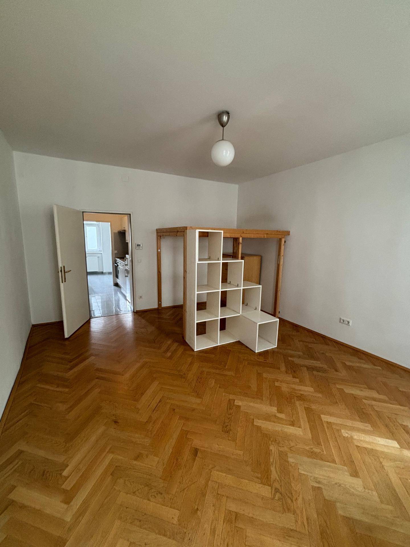 Helles Zimmer mit Holzparkett und einer multifunktionalen Hochbett-Regal-Kombination, gut beleuchtet.