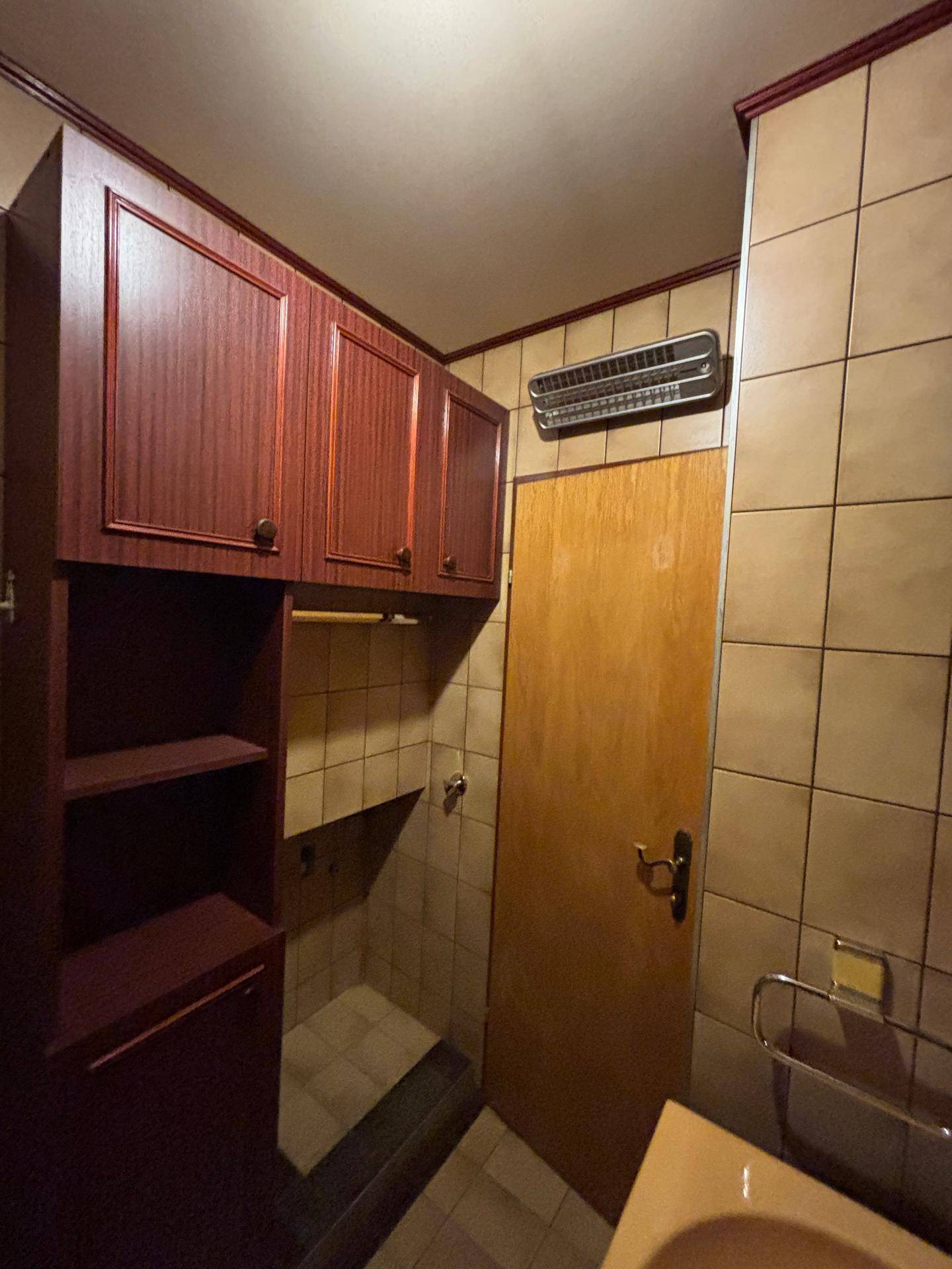 Badezimmerbereich mit Duschkabine, Fliesenwänden und praktischen Holzschränken für Stauraum.
