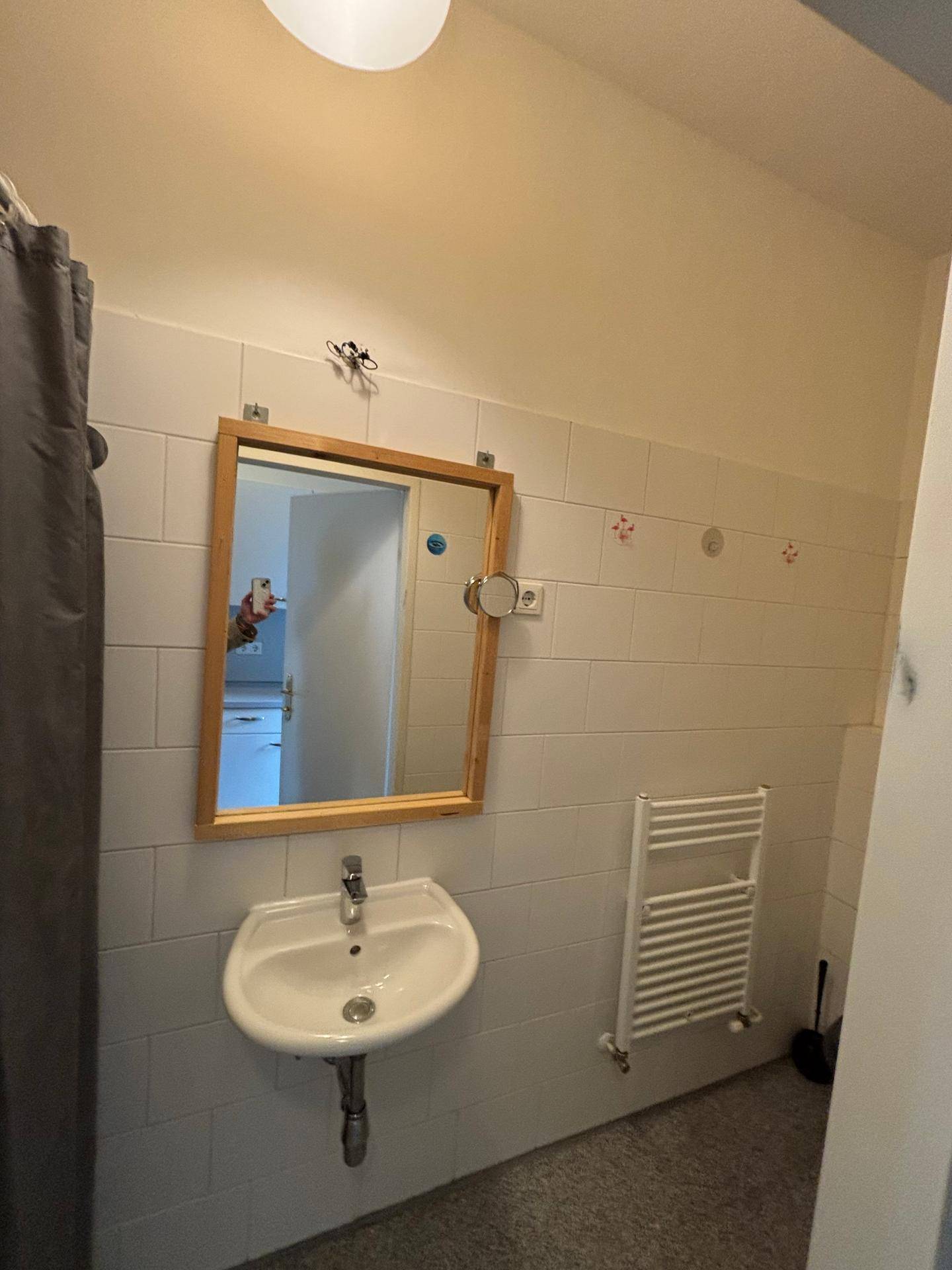 Badezimmer mit Waschbecken, Spiegel und beheiztem Handtuchhalter, hell gefliest und funktional.