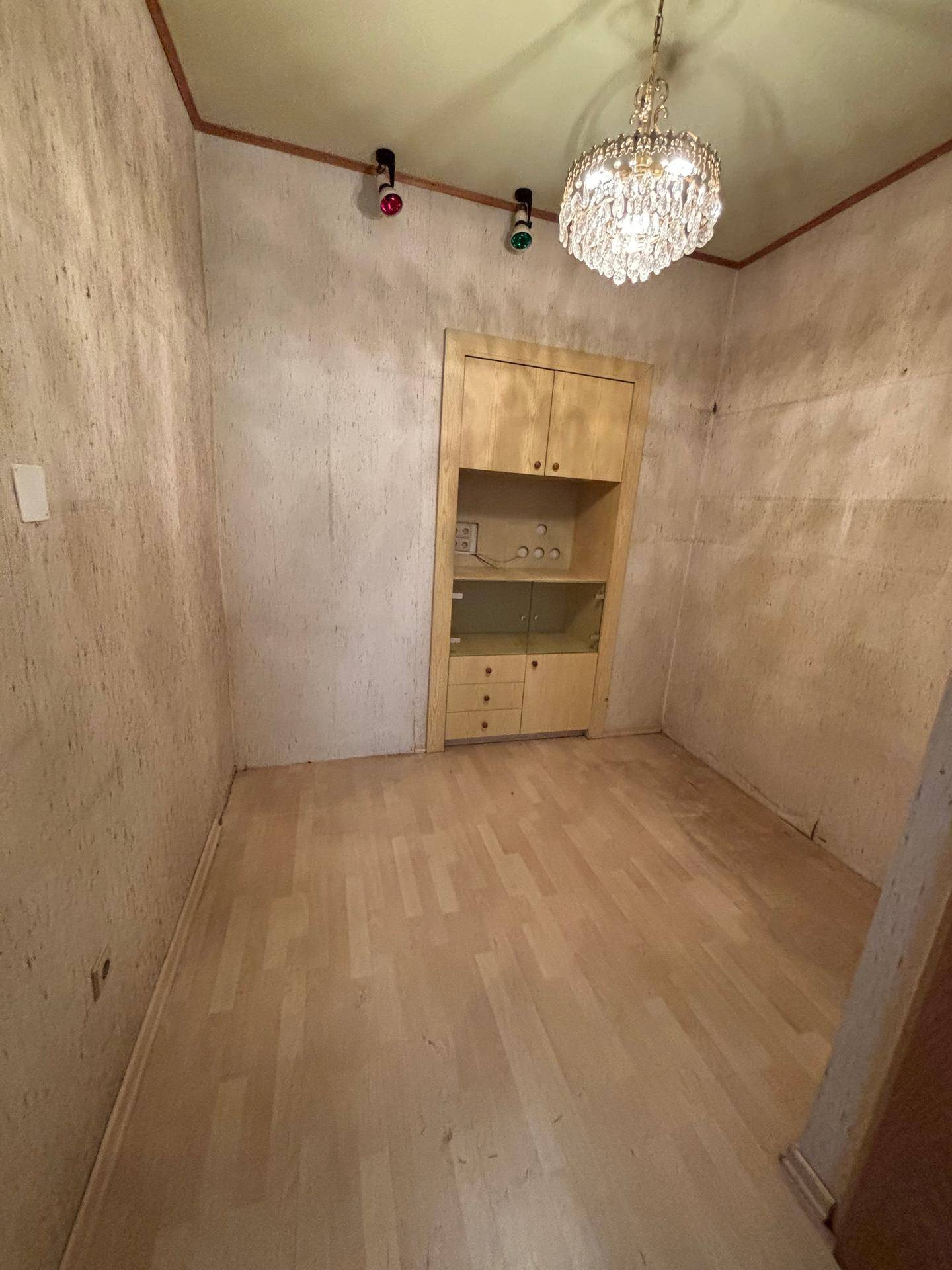 Leeres Zimmer mit hellem Laminatboden, strukturierten Wänden und einem eleganten Kronleuchter.