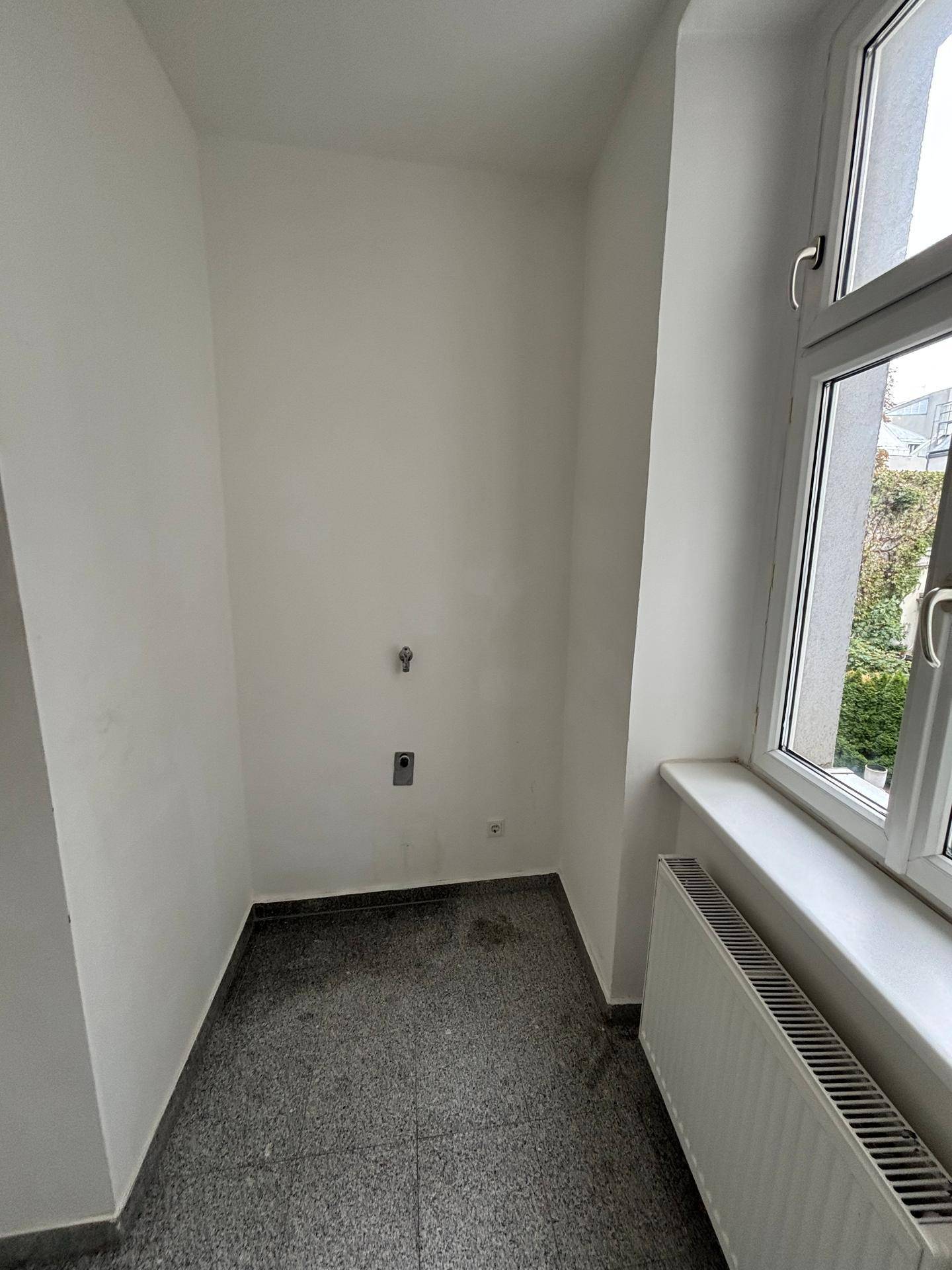 Kleiner Hauswirtschaftsraum mit Fliesenboden, Fenster und Anschlüssen für Waschmaschine.