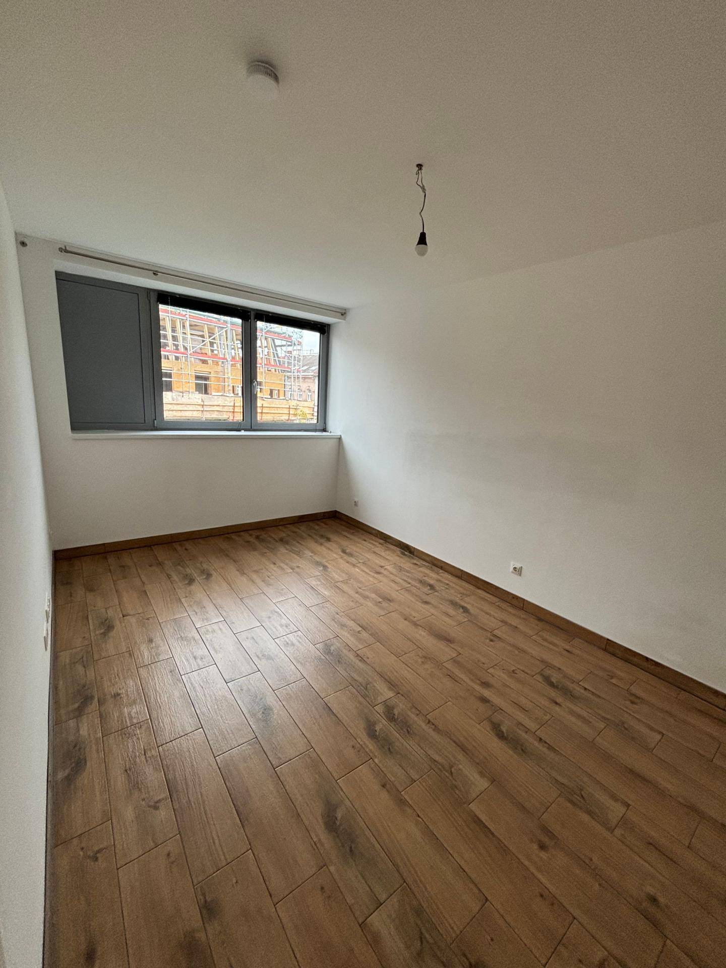 Leeres Schlafzimmer mit Holzboden und einem Fenster, das den Blick auf eine Baustelle freigibt.