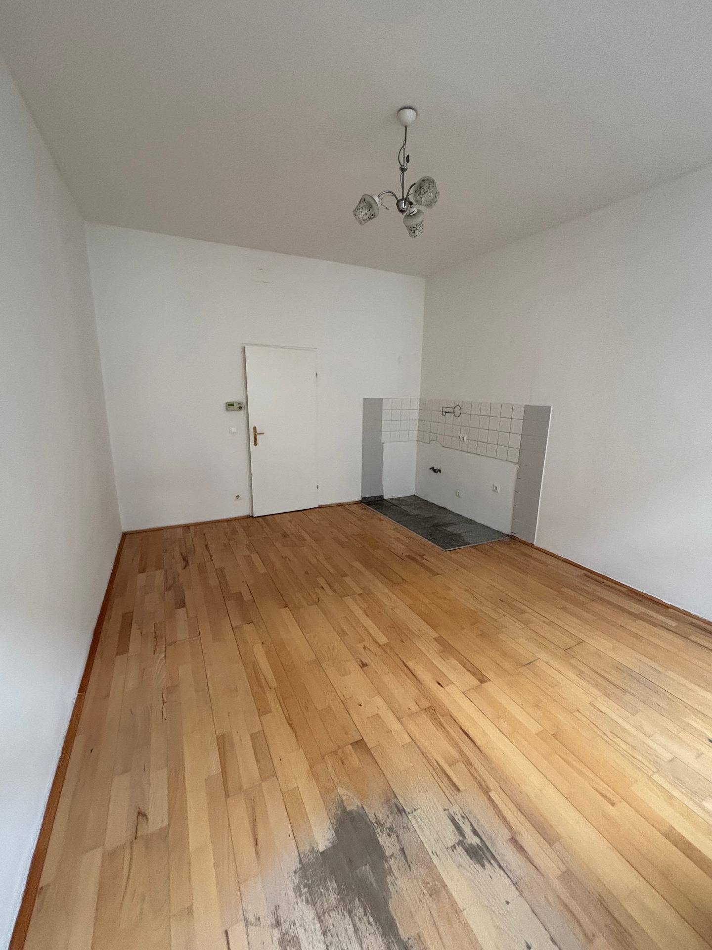 Leerer Raum mit Holzplankenboden, weißen Wänden und vorbereiteter Nische für eine Küchenzeile.