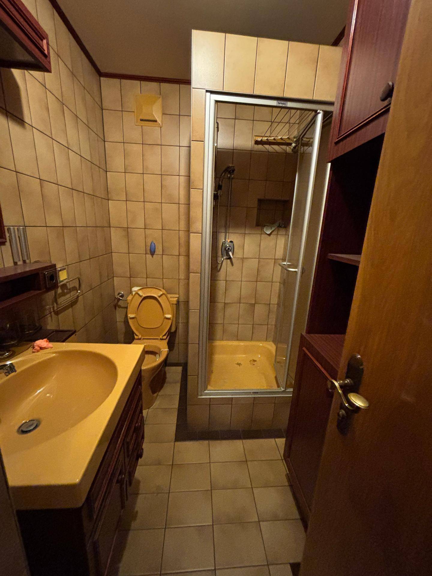 Badezimmer mit beigen Fliesen, Duschkabine und Toilette in warmen Farbtönen der 80er Jahre.
