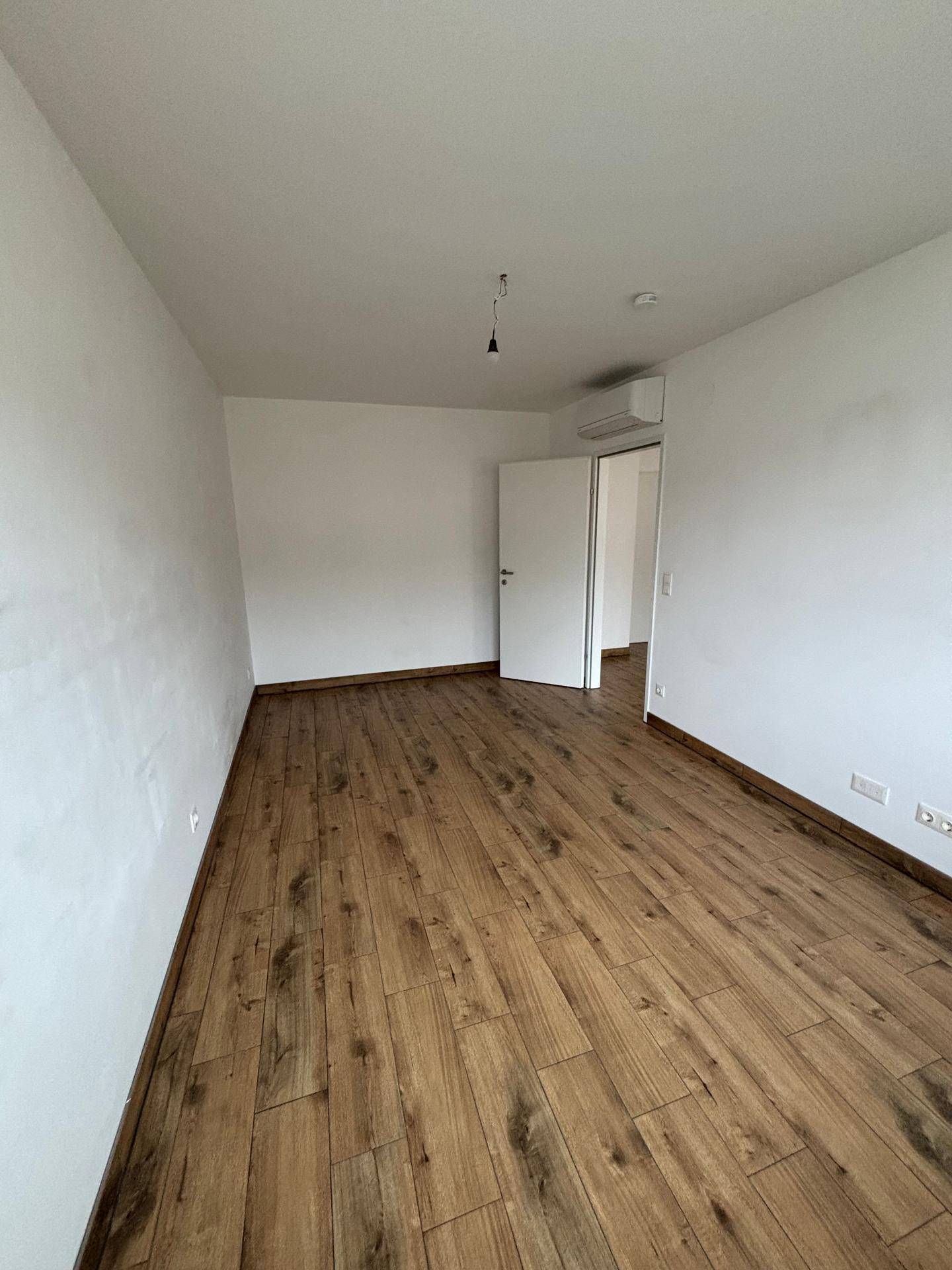 Helles Schlafzimmer mit Holzboden, weißen Wänden und einer installierten Klimaanlage.