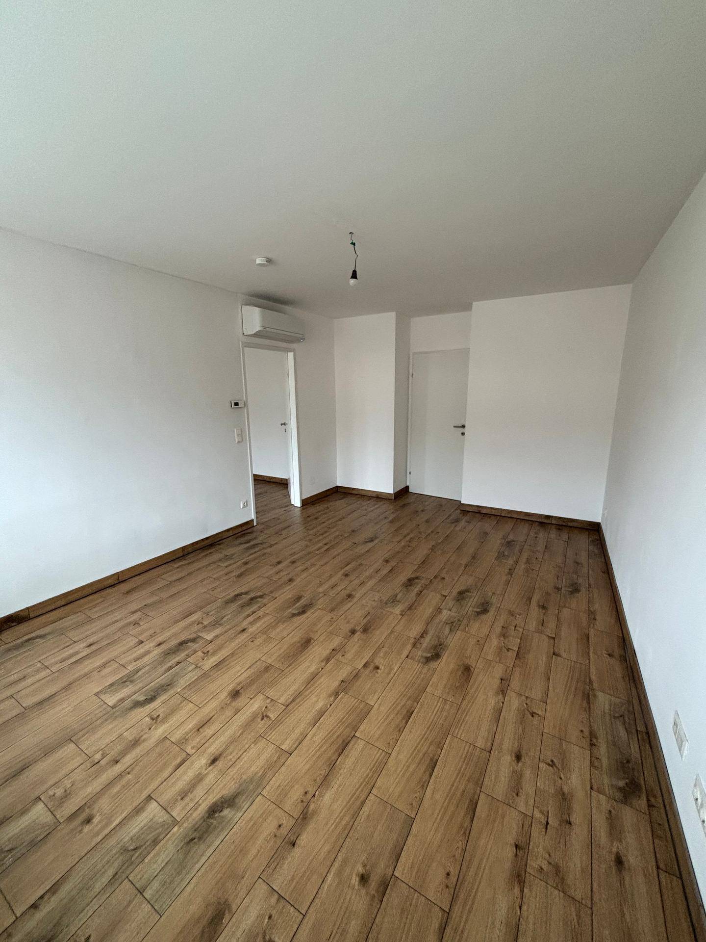 Heller Wohnraum mit Holzboden, weißen Wänden und einer Klimaanlage für angenehmes Raumklima.