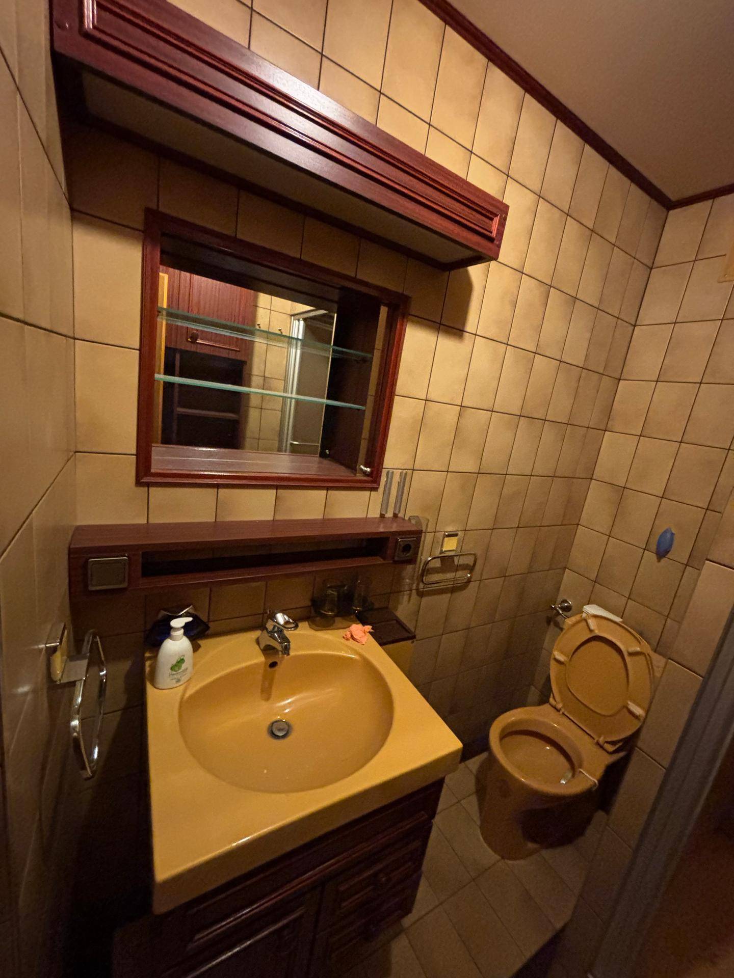 Badezimmer mit beigen Fliesen, Waschbecken mit Unterschrank und passendem Spiegelschrank.