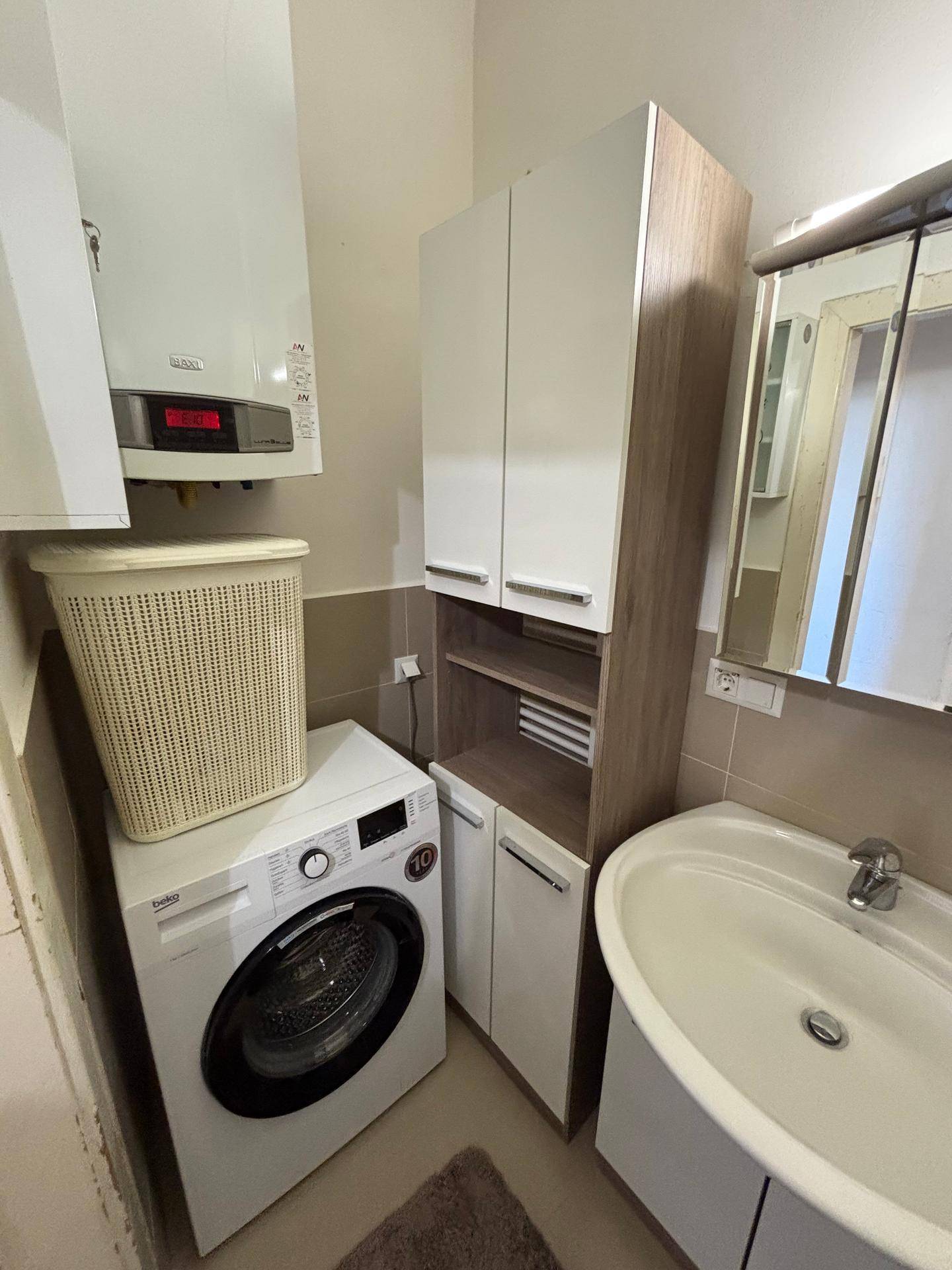 Funktionales Badezimmer mit Waschmaschine, Waschbecken und Hängeschränken, inklusive Warmwasserbereiter.