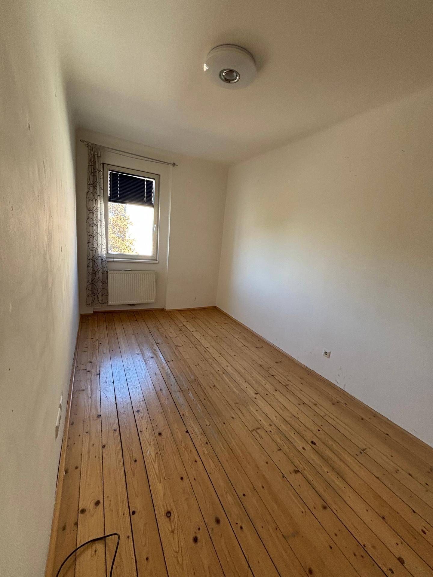 Helles Schlafzimmer mit Holzdielenboden und einem Fenster, das viel Tageslicht hereinlässt.