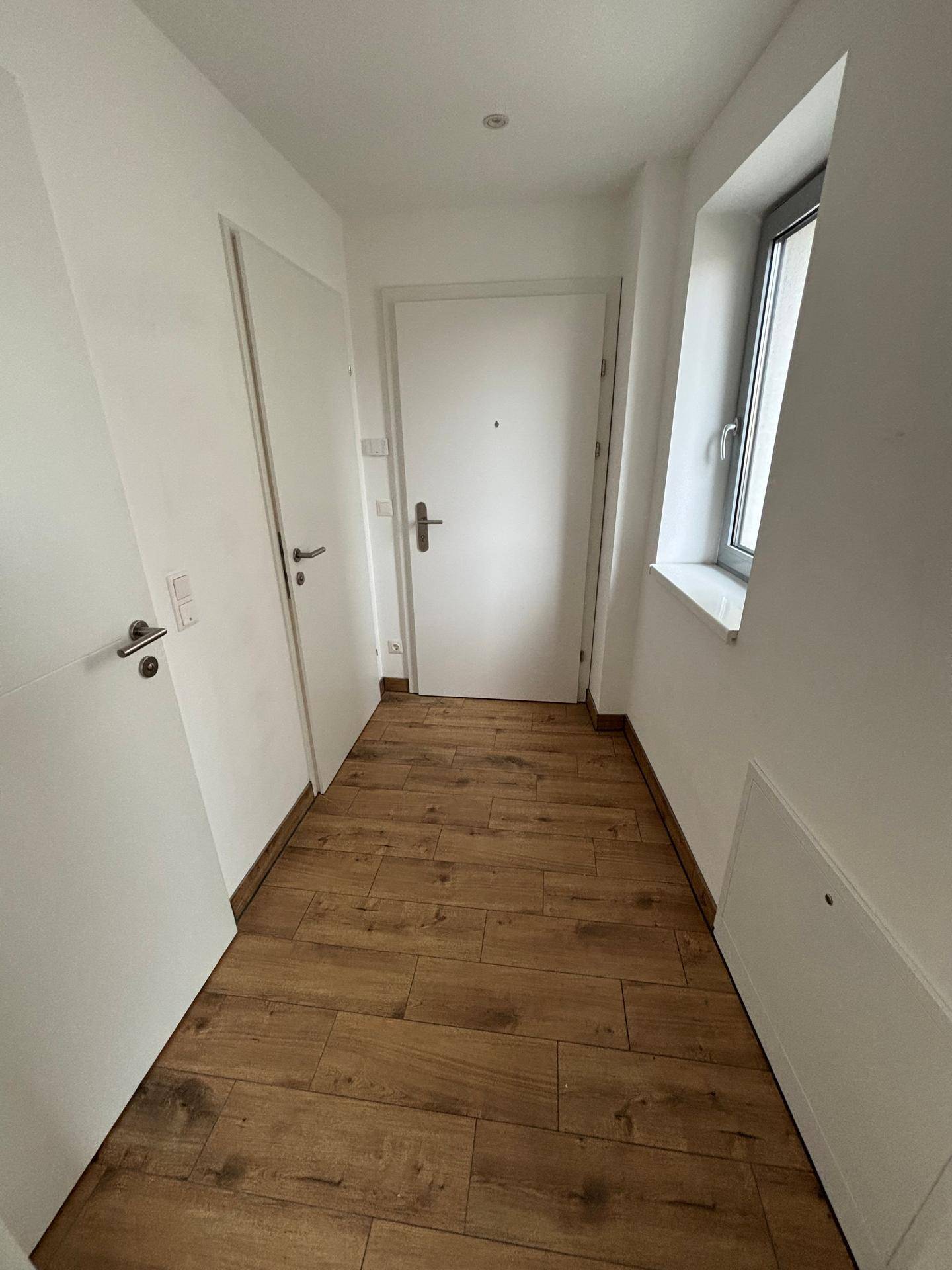 Eingangsbereich mit Holzboden, weiß gestrichenen Wänden und einem Fenster für Tageslicht.