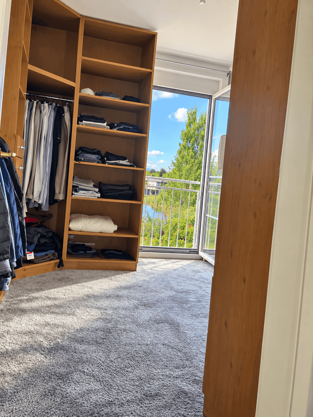 Begehbarer Kleiderschrank mit Holzregalen und Zugang zu einem französischen Balkon.