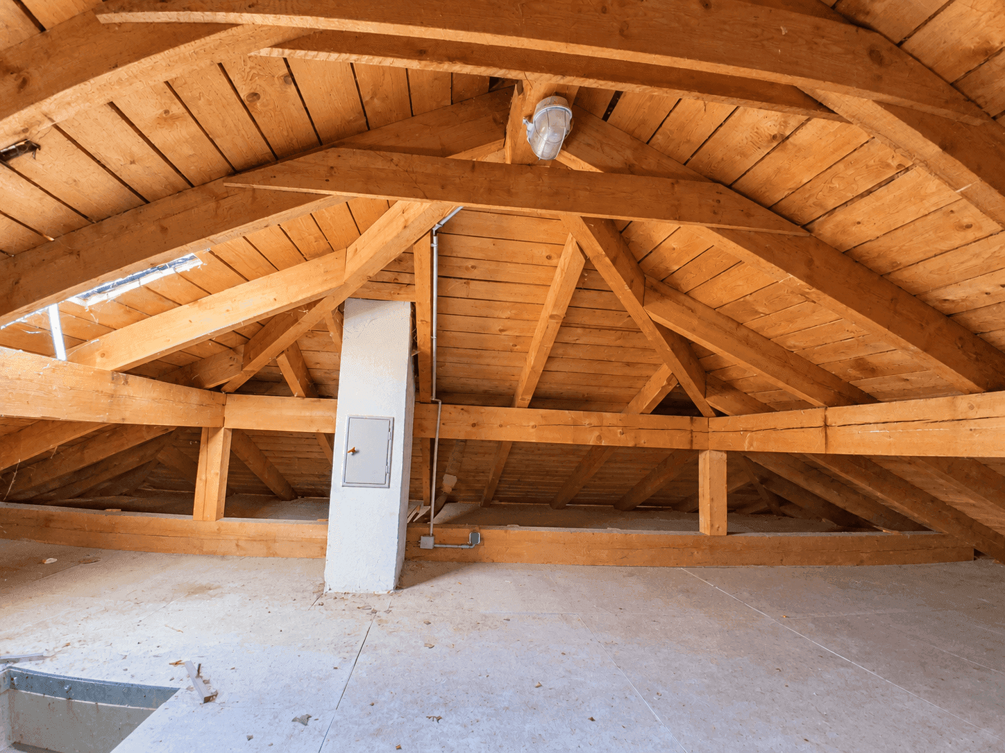 Unausgebauter Dachboden mit sichtbaren Holzbalken und Betonboden, bereit für den Ausbau.