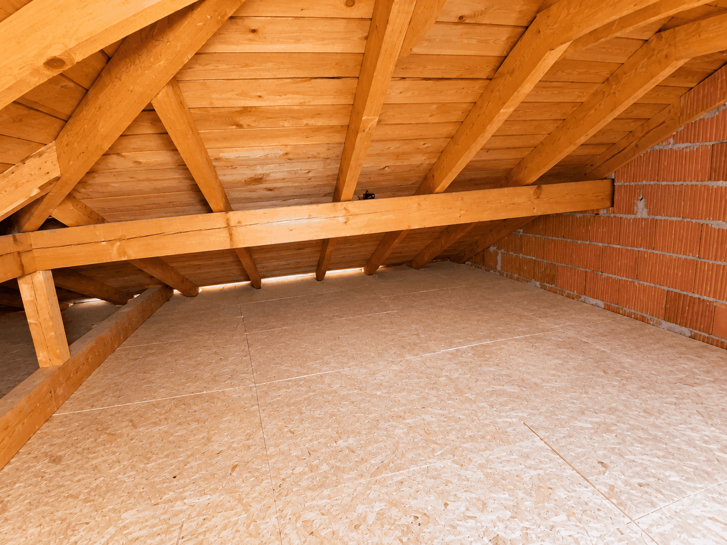 Dachboden mit sichtbarer Holzkonstruktion und Ziegelwand, mit OSB-Platten ausgelegt.