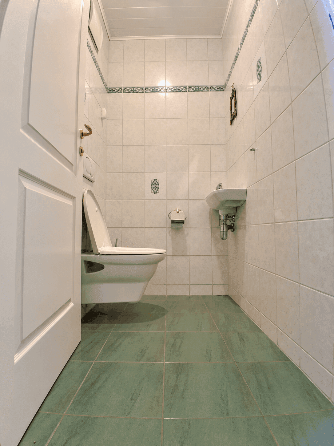 Kleines Gäste-WC mit Wand-WC und Handwaschbecken, gefliest in Grün und Weiß.