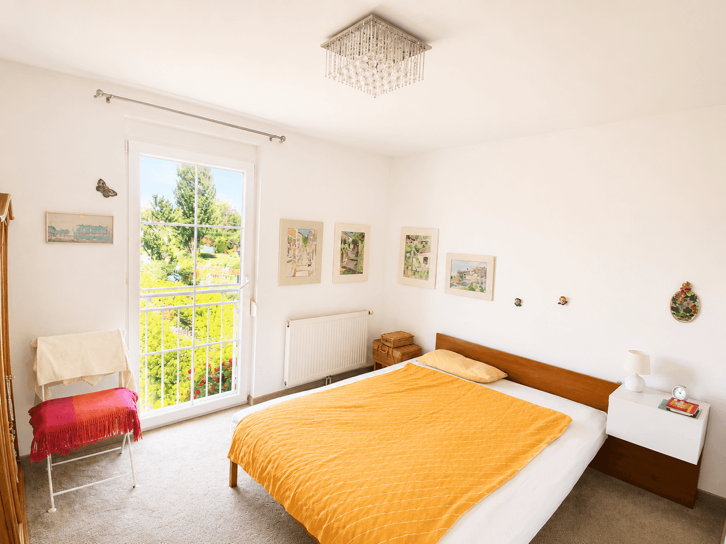 Helles Schlafzimmer mit Teppichboden, Einzelbett und französischem Balkon mit Grünblick.