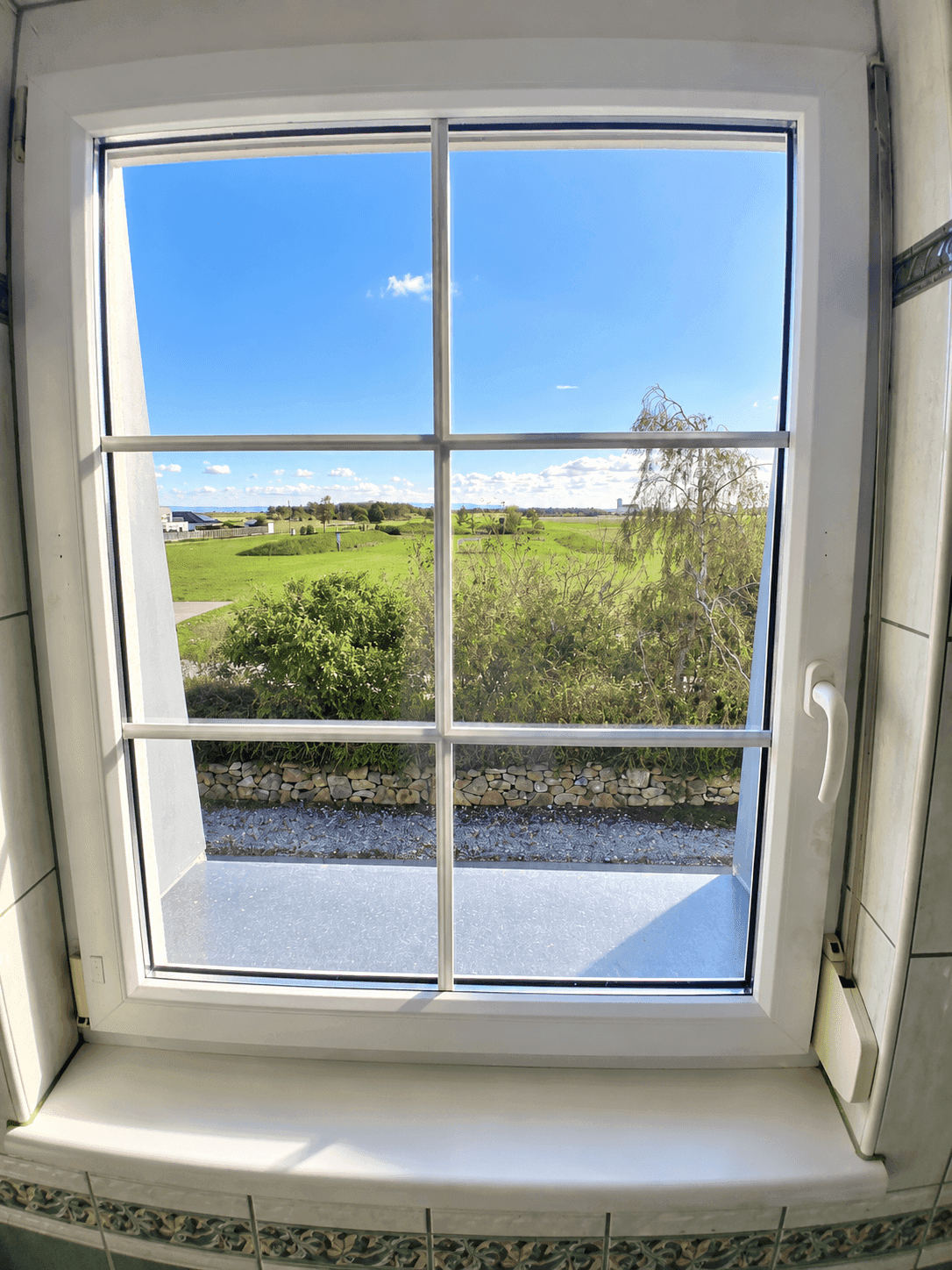 Weitblick aus dem Fenster auf eine grüne Landschaft unter blauem Himmel.