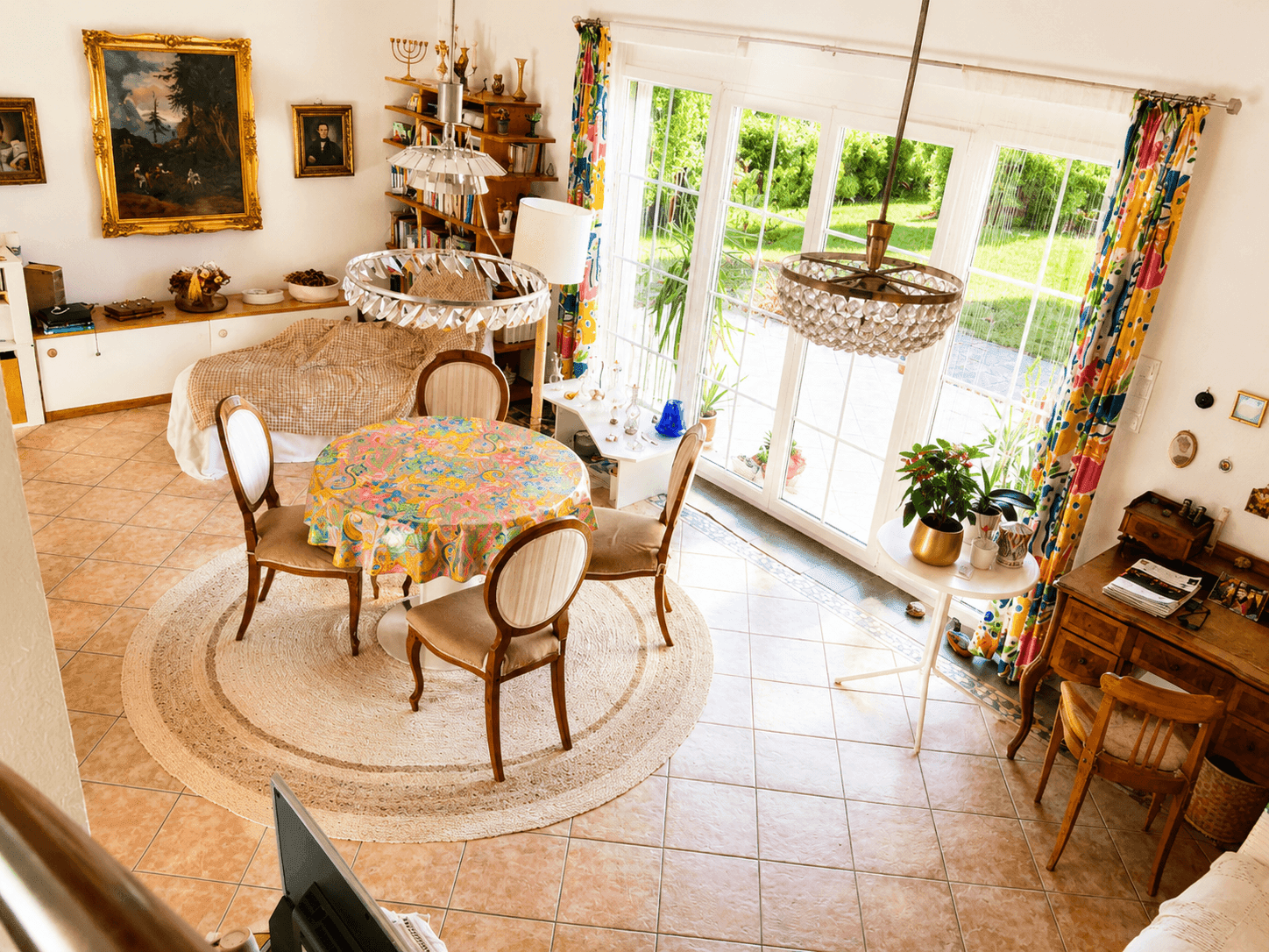Heller Wohn- und Essbereich mit Fliesenboden, bunten Vorhängen und Zugang zum Garten.