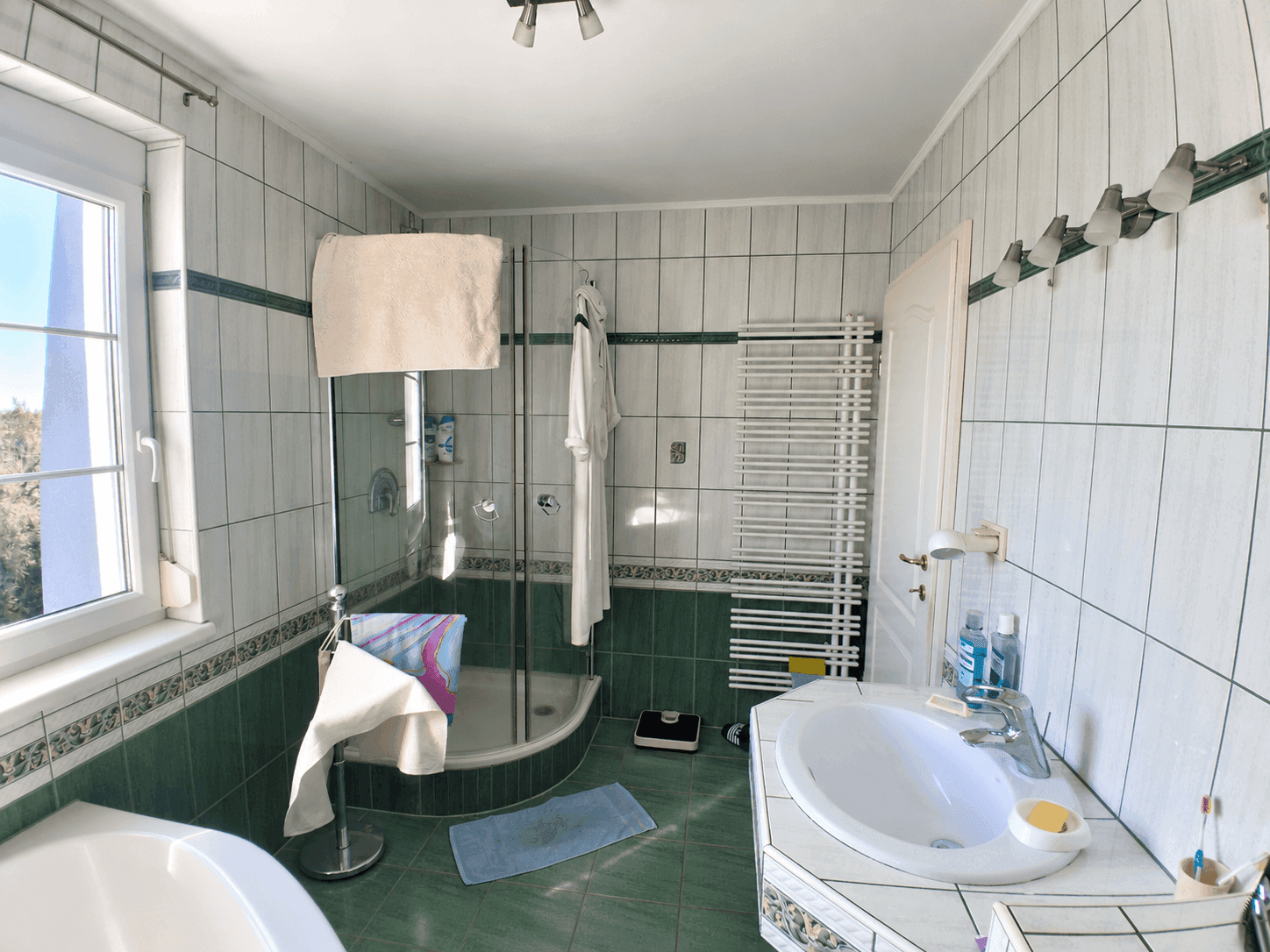 Geräumiges Badezimmer mit Duschkabine, Waschbecken und Fenster, gefliest in Grün und Weiß.
