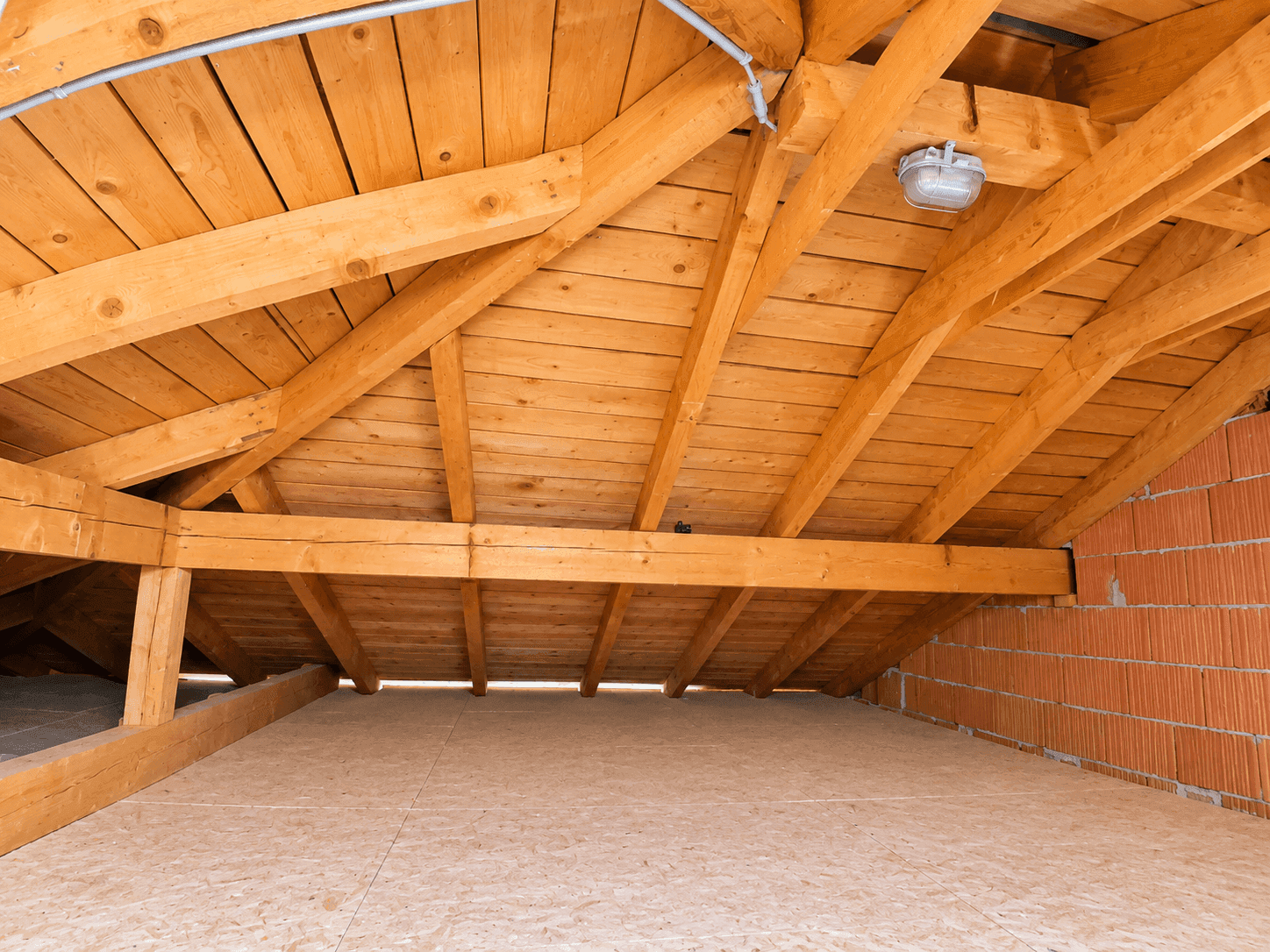 Unausgebauter Dachboden mit sichtbaren Holzbalken und Ziegelmauerwerk.