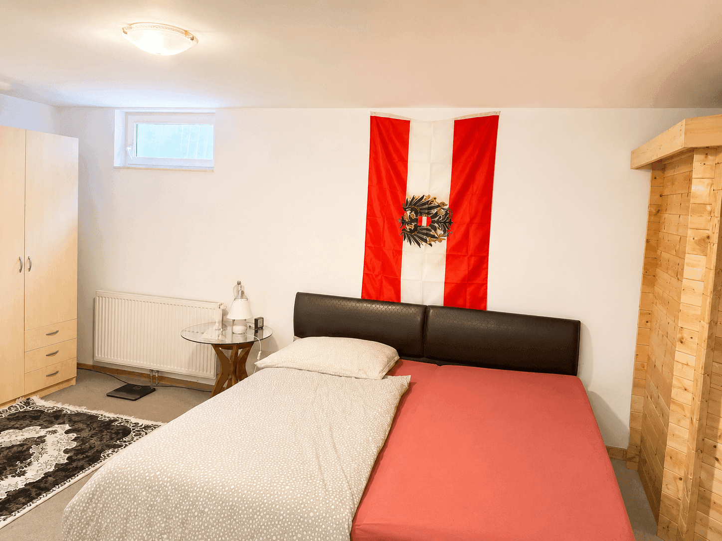 Schlafzimmer mit Doppelbett, Kleiderschrank und einem kleinen Fenster im Untergeschoss.