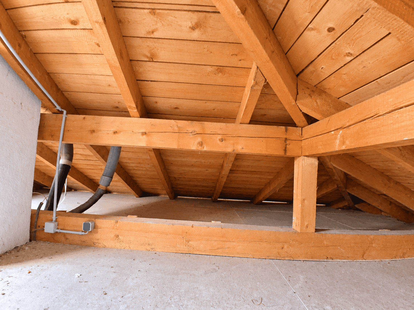 Dachboden mit sichtbaren Holzbalken, Rohrleitungen und Betonboden, bereit für den Ausbau.