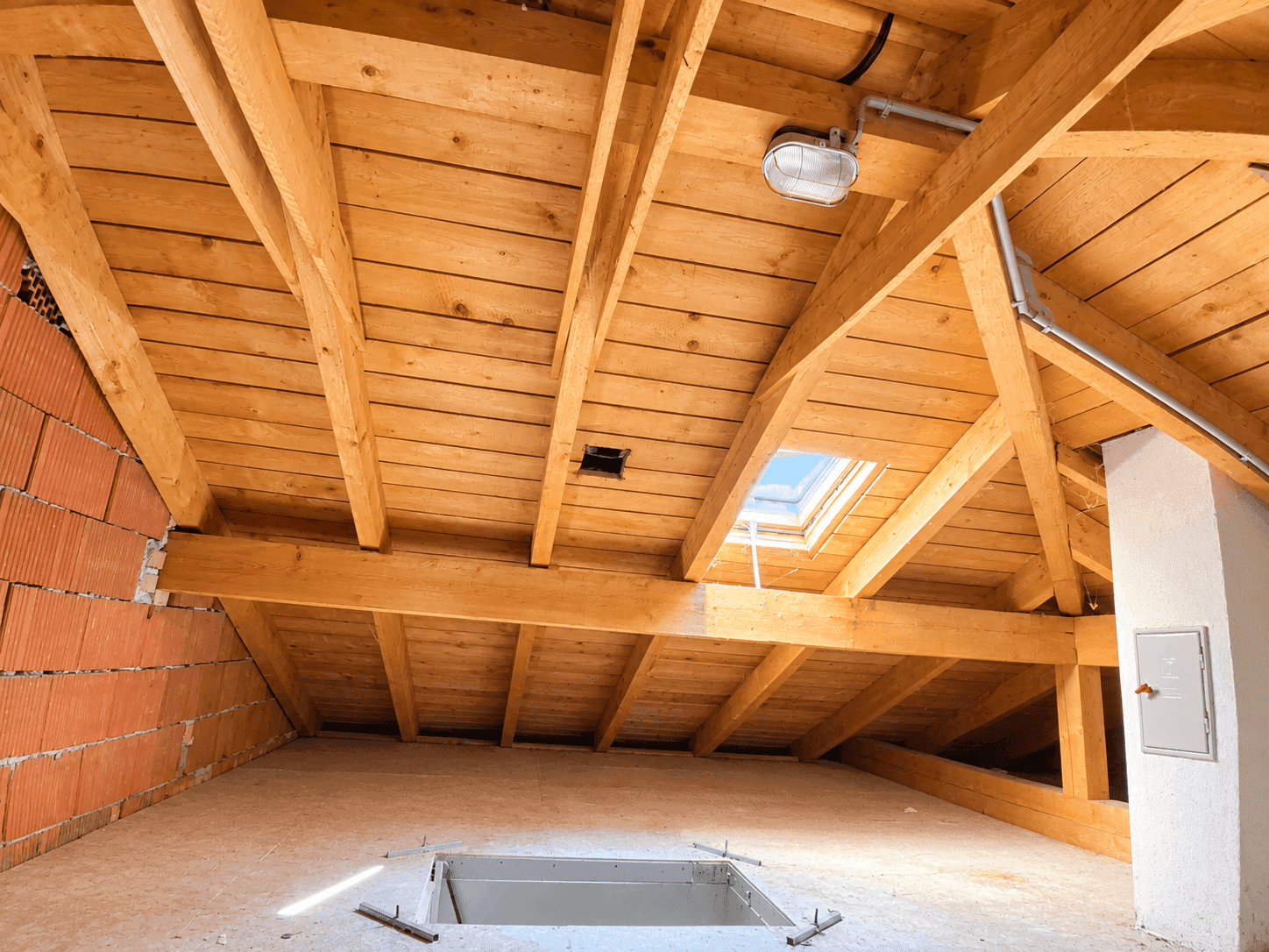 Dachboden mit sichtbarer Holzkonstruktion, Dachfenster und unverputzter Ziegelwand.