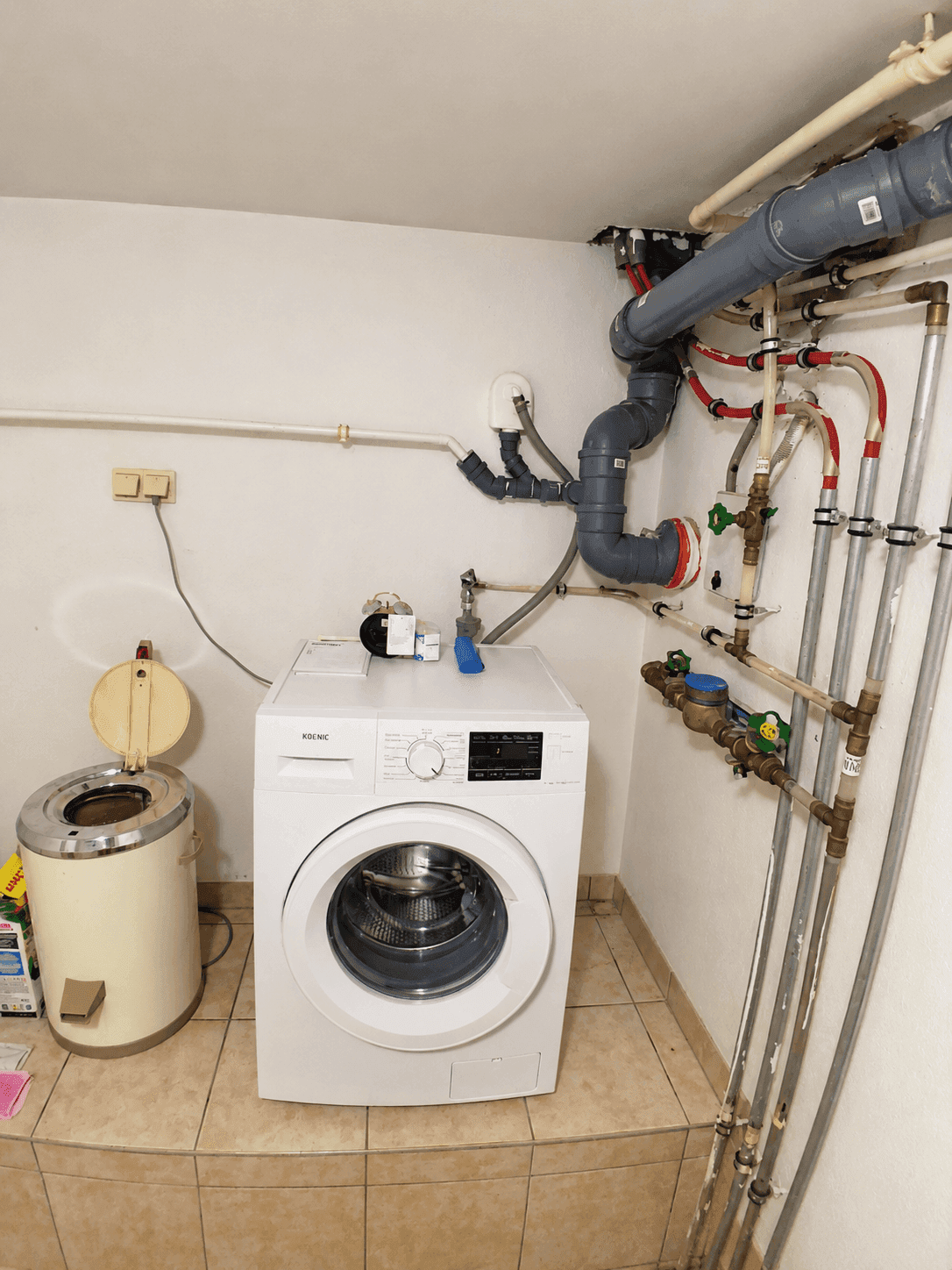 Hauswirtschaftsraum mit Waschmaschine, sichtbaren Rohrleitungen und Fliesenboden.