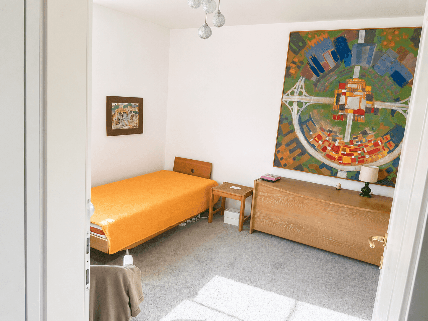 Schlafzimmer mit Teppichboden, Einzelbett und einem großen, farbenfrohen Wandgemälde.