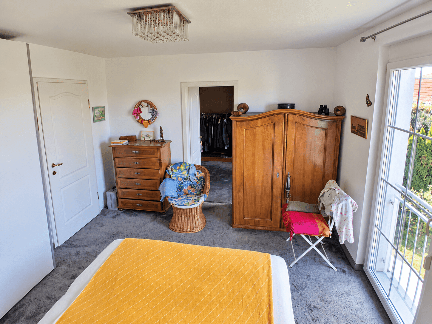Schlafzimmer mit Doppelbett, Holzschrank und Zugang zu einem französischen Balkon.