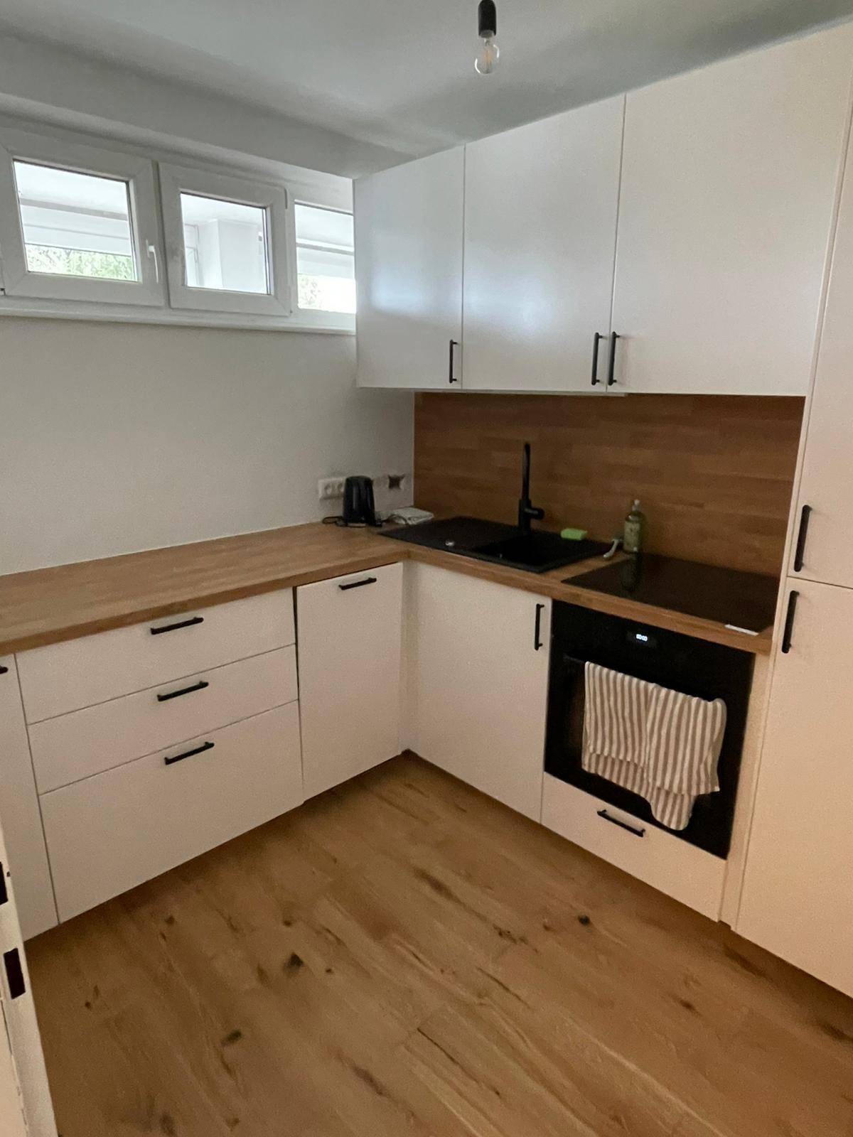 Moderne Einbauküche mit weißen Schränken, Holz-Arbeitsplatten und Fenster für Tageslicht.