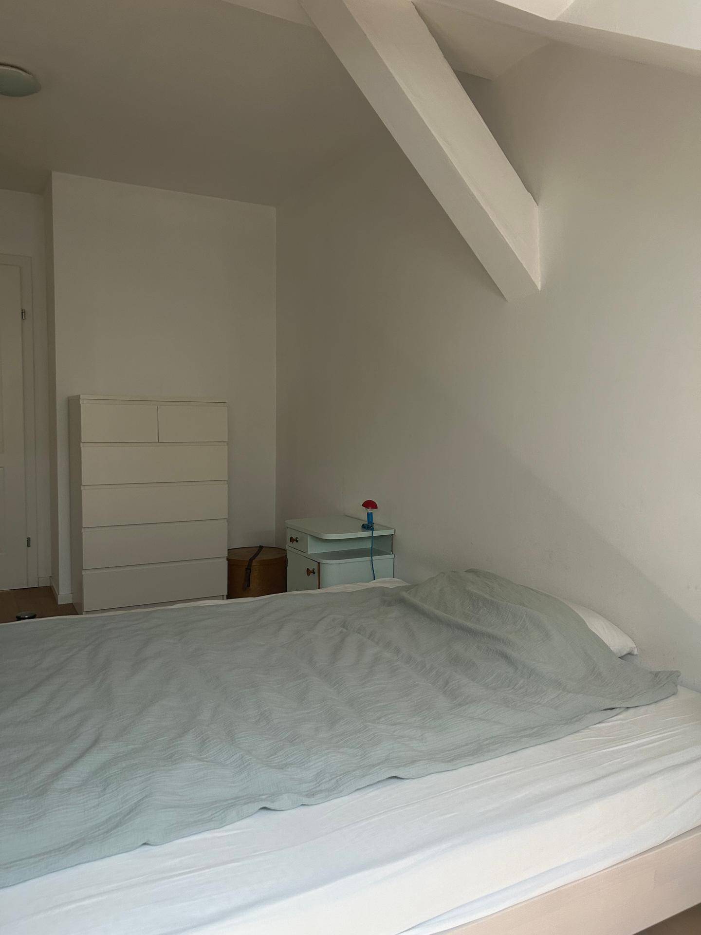 Schlafzimmer im Dachgeschoss mit schräger Decke, Holzbalken und einfacher Einrichtung.