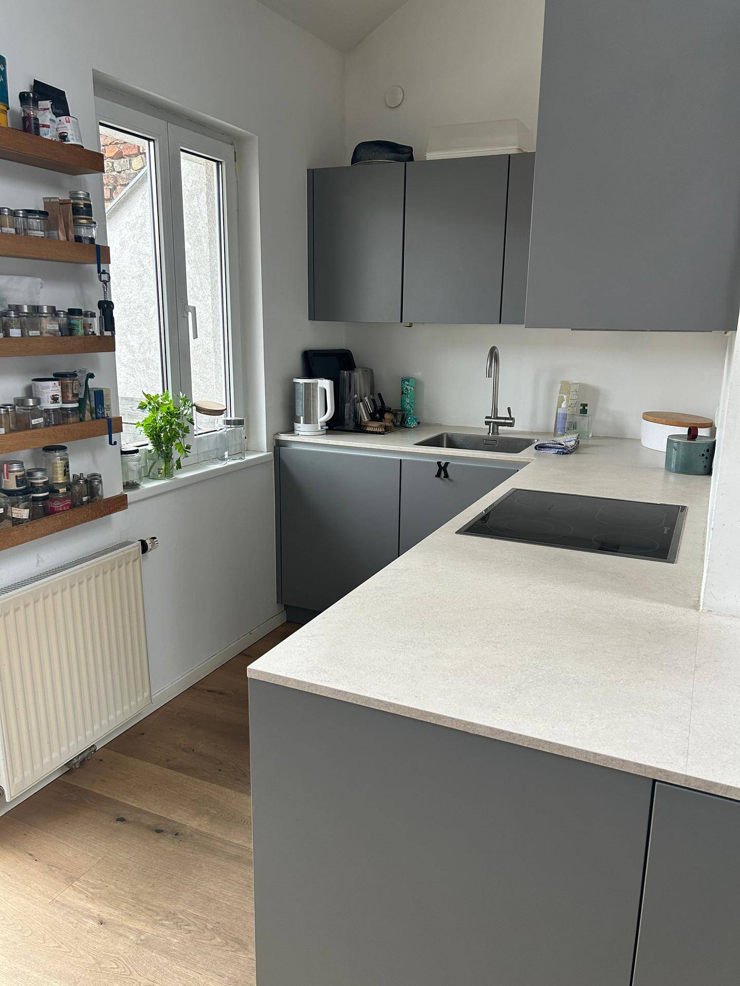 Moderne Küche mit grauen Schränken, heller Arbeitsplatte, Induktionskochfeld und Fenster.