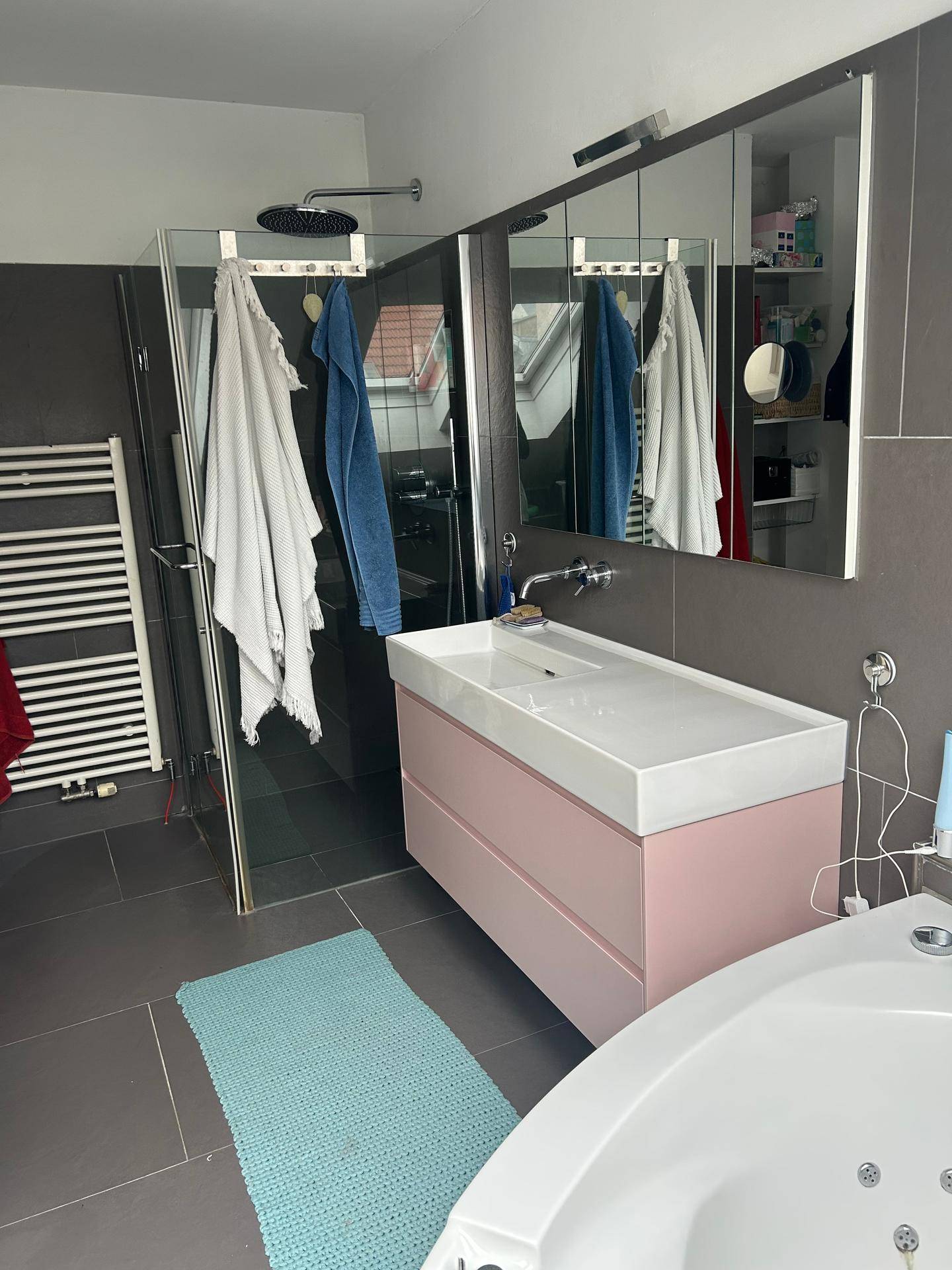 Modernes Badezimmer mit grauen Fliesen, rosa Waschtisch, Duschkabine und Eckbadewanne.