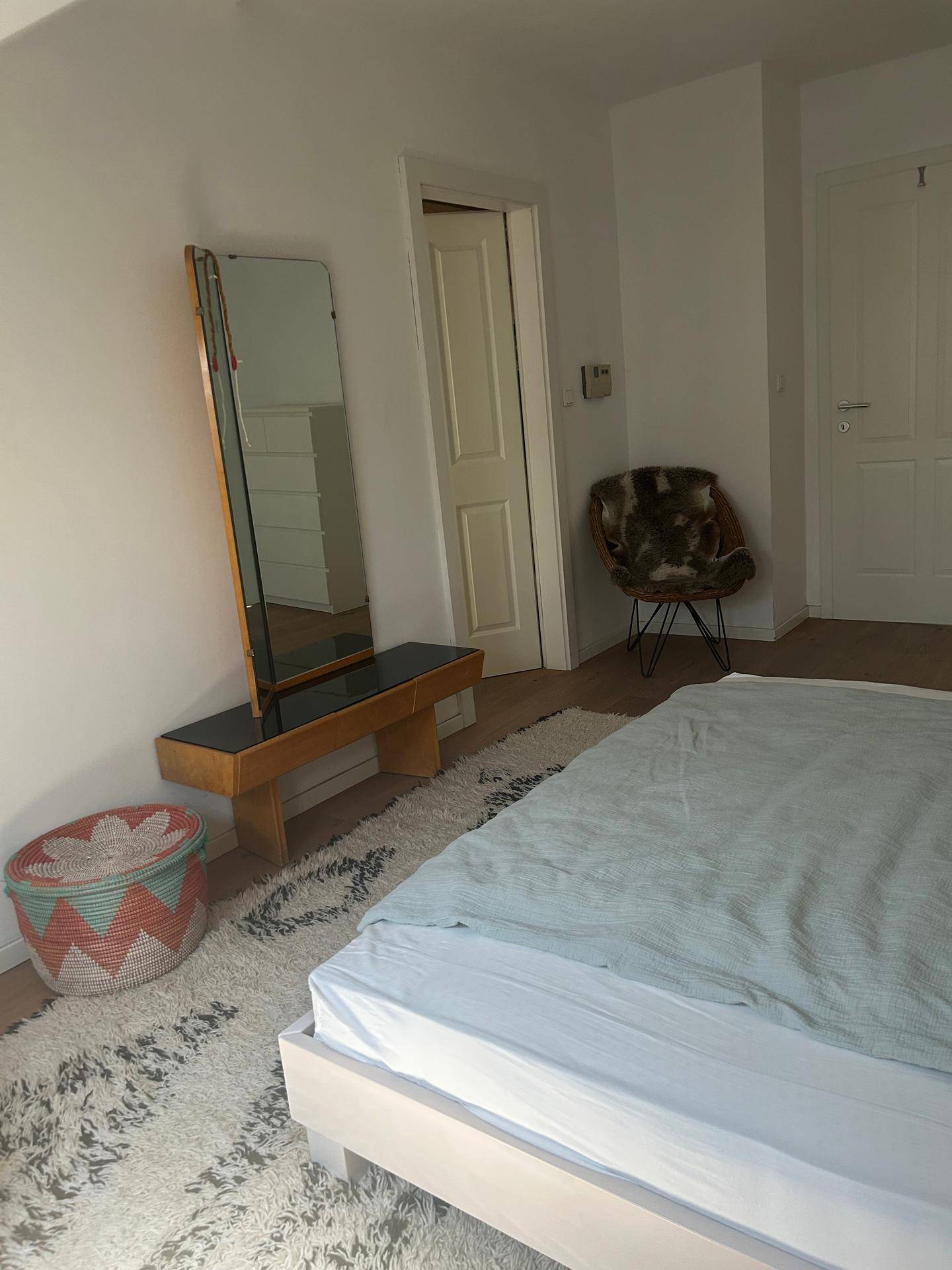 Schlafzimmer mit Holzboden, großem Spiegel und einem dekorativen Sessel.