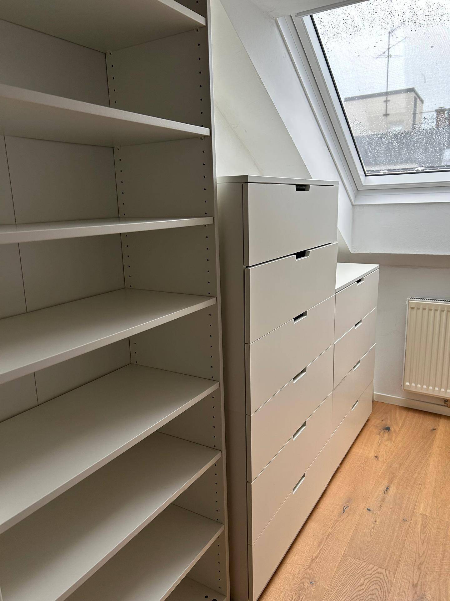 Praktischer Abstellraum mit Regalen und Schubladen unter einer Dachschräge mit Fenster.